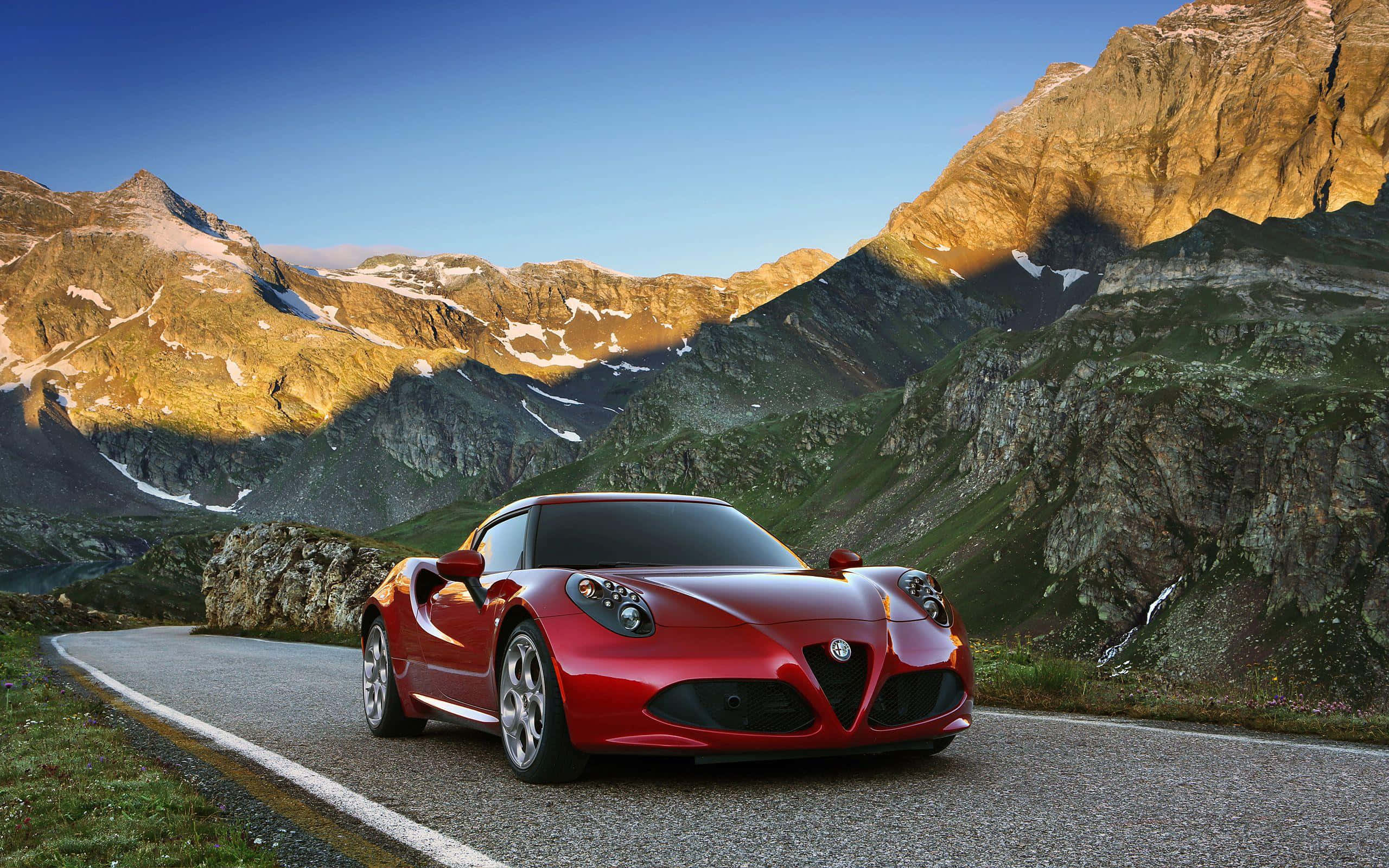 Alfa Romeo 4c 桌布 壁紙 — 一輛充滿活力的紅色愛快羅密歐跑車沿著蜿蜒的山路行駛，沐浴在金色的夕陽光芒中。