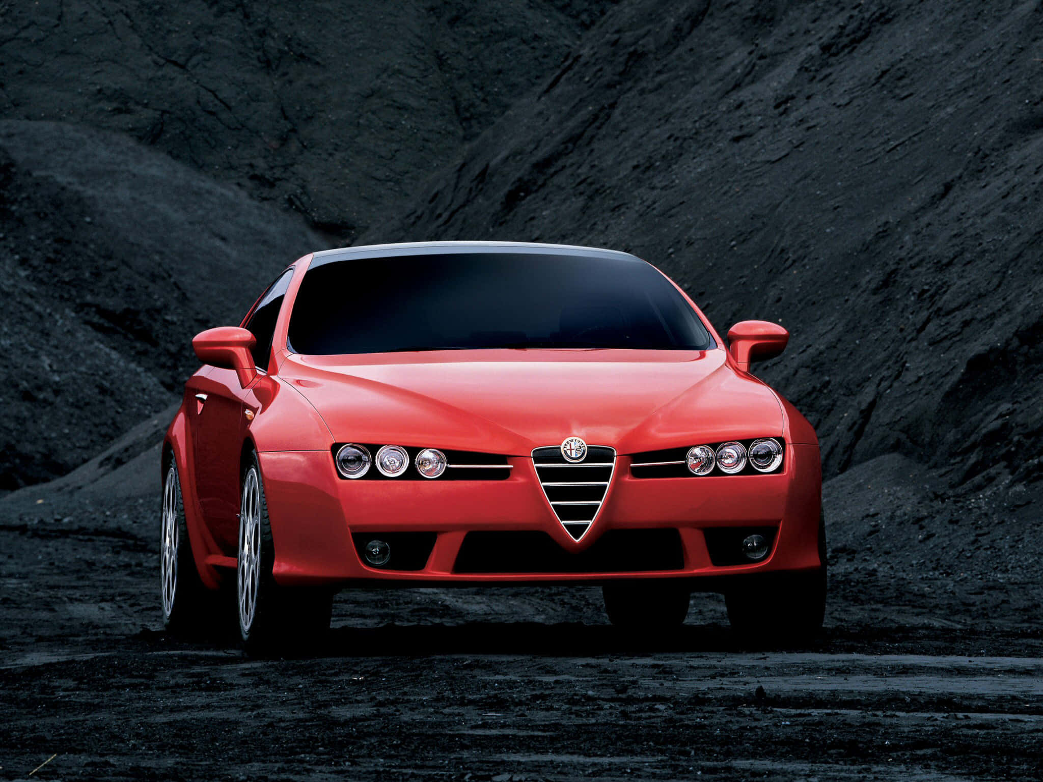 Alfa Romeo Brera 桌布 壁紙 — 一輛充滿活力的紅色愛快羅密歐跑車，在黑色火山岩背景下蓄勢待發。