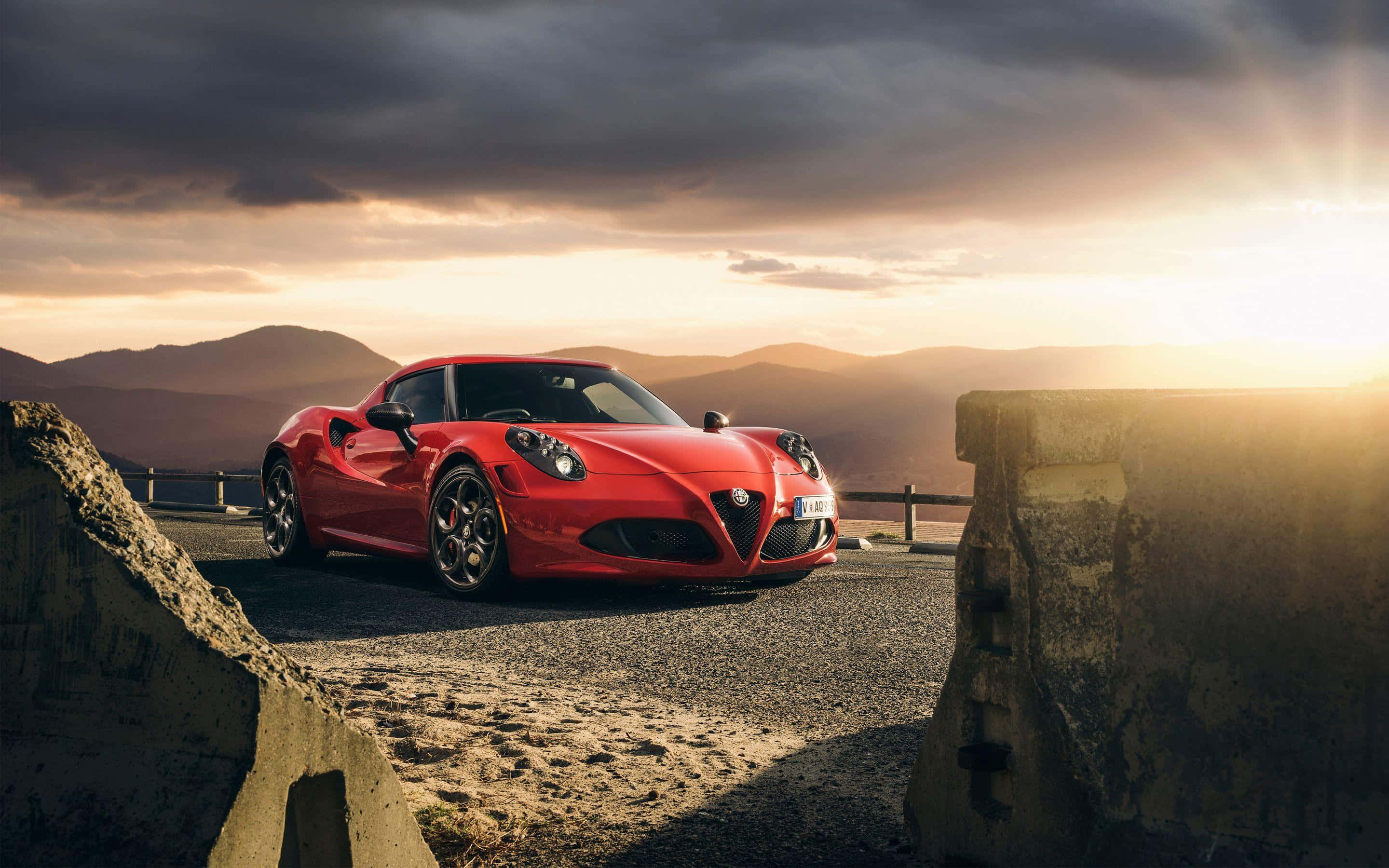 Alfa Romeo 4c 桌布 壁紙 — 一輛充滿活力的紅色愛快羅密歐跑車停在日落時分的山路上，背景有戲劇性的雲層和遠山。