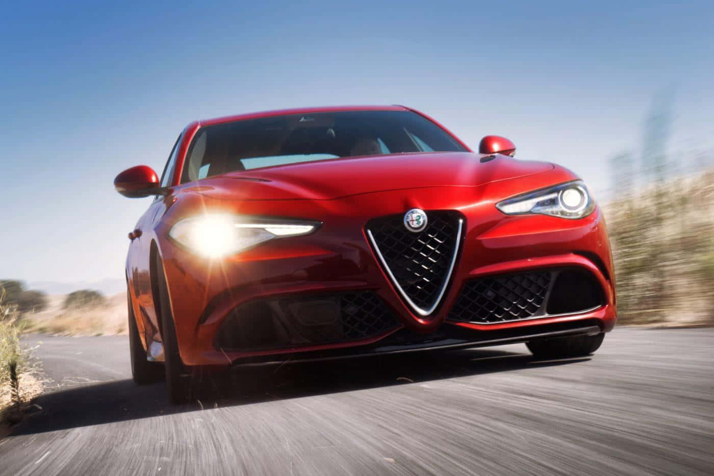 Alfa Romeo Giulia 桌布 壁紙 — 一輛充滿活力的紅色愛快羅密歐跑車在晴朗的藍天下，沿著沙漠公路疾馳，動態模糊強調了速度。