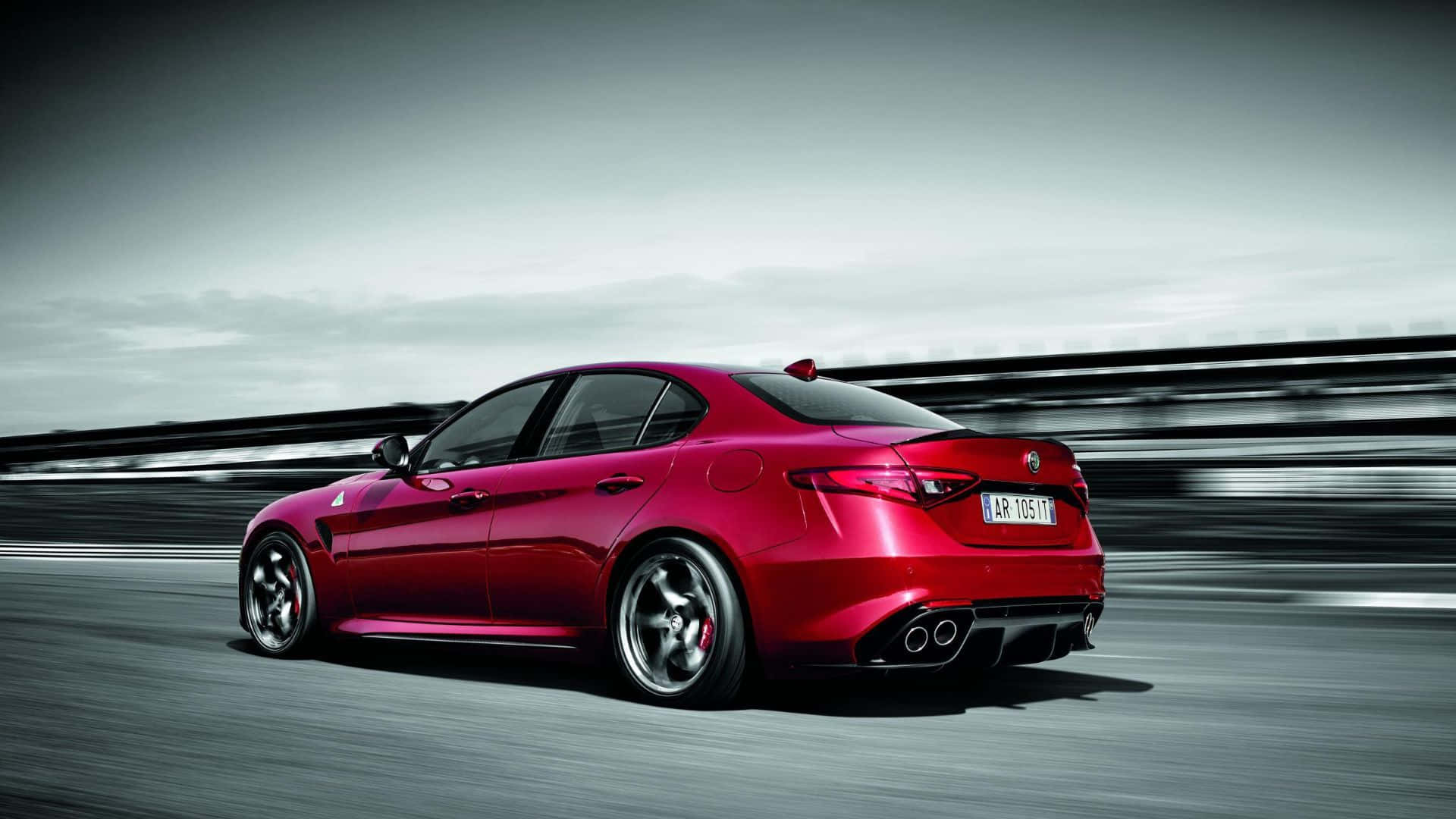 Alfa Romeo Giulia 桌布 壁紙 — 一輛充滿活力的紅色愛快羅密歐轎車在陰天下的模糊賽道上疾馳。
