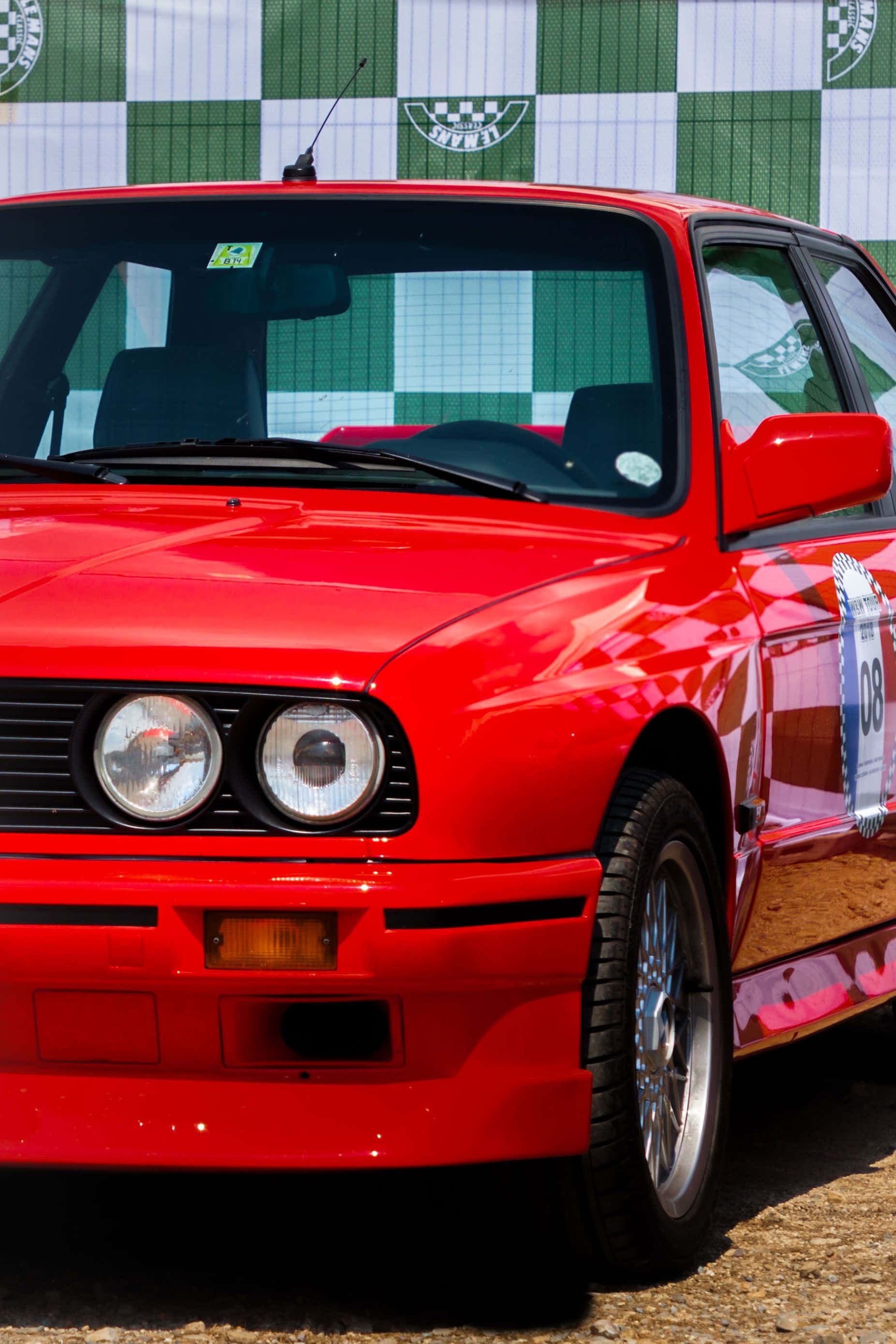 Bmw Cars 桌布 壁紙 — 一輛充滿活力的紅色拉力賽車，帶有賽車貼紙和格子旗背景，在明亮的陽光下閃閃發光。