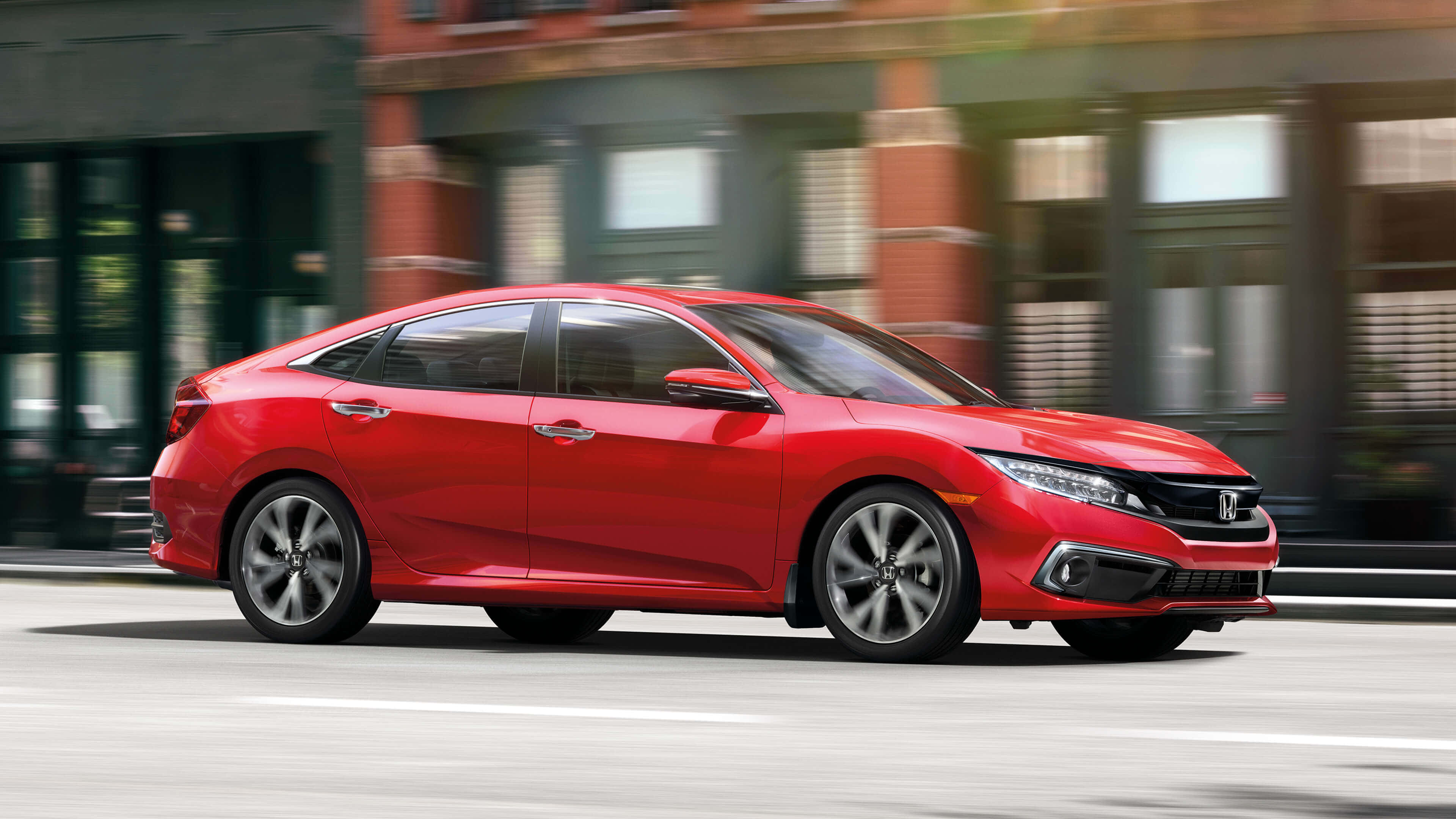Honda Civic 桌布 壁紙 — 一輛充滿活力的紅色本田思域房車在城巿街道上飛馳，背景中的城巿建築物呈現動態模糊效果。