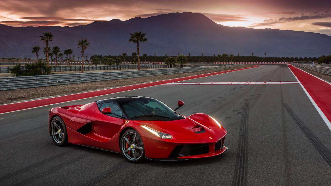 跑車 桌布 壁紙 — 一輛充滿活力的紅色法拉利 LaFerrari 在日落時分沿著賽道飛馳，背景有棕櫚樹和山脈。