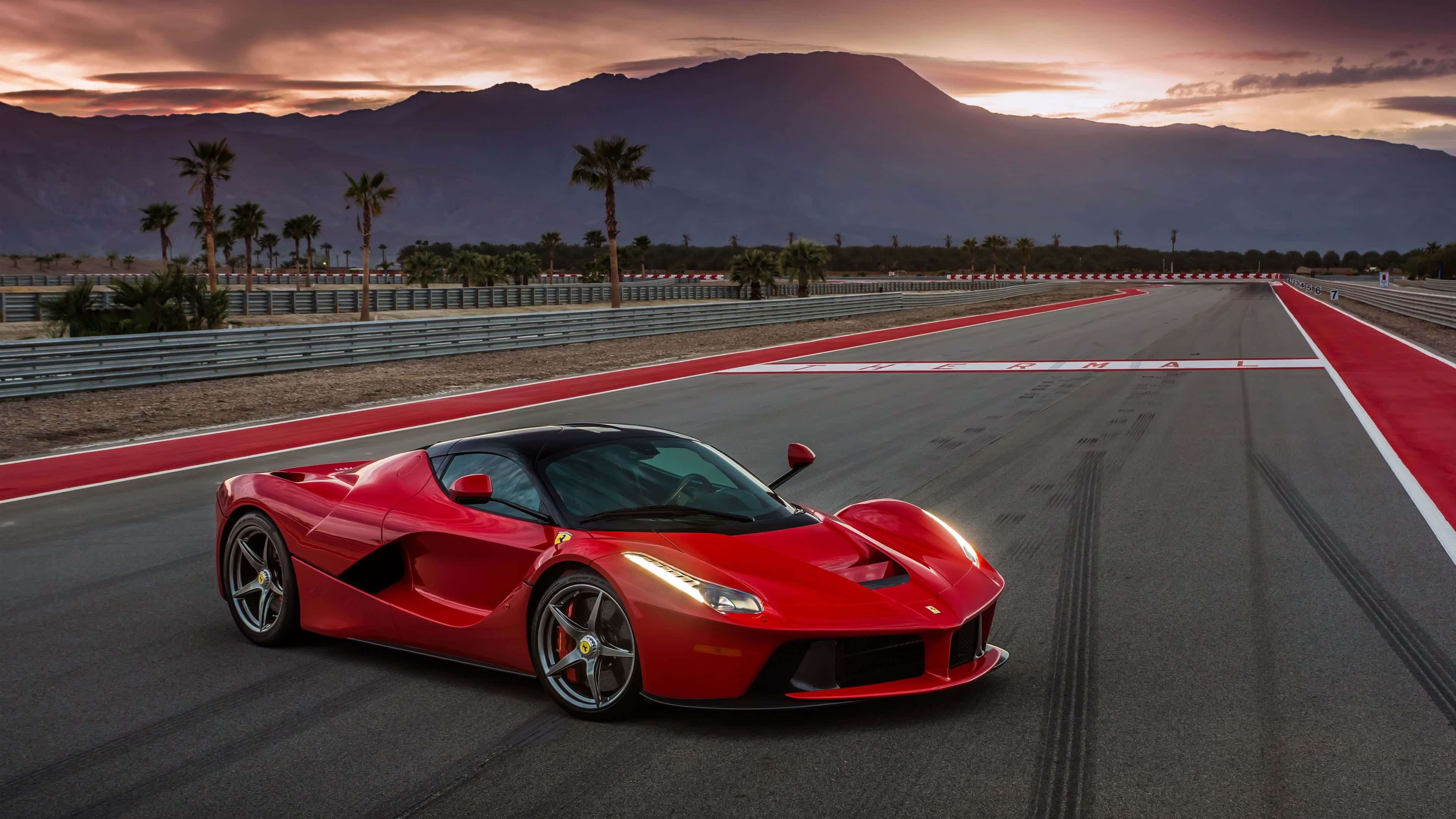 4K 法拉利 桌布 壁紙 — 一輛充滿活力的紅色法拉利 LaFerrari 在沙漠賽道上奔馳，背景是棕櫚樹和山脈，夕陽西下。