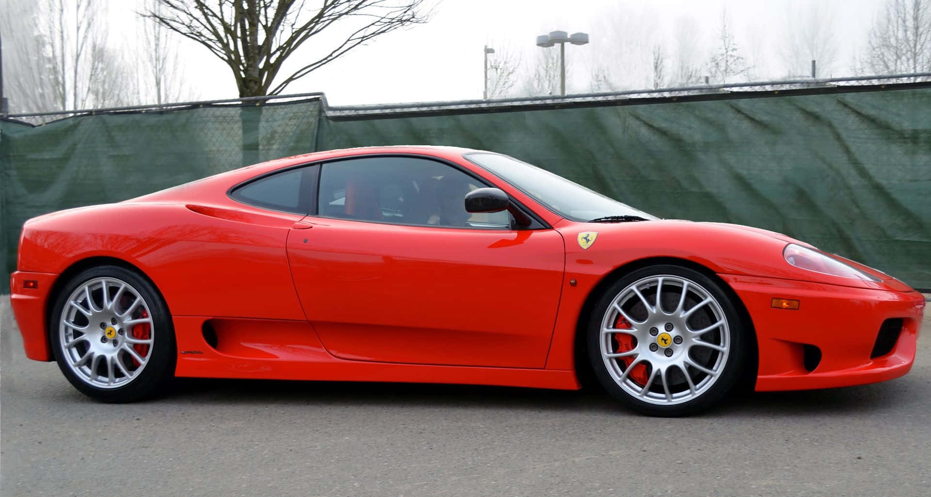Ferrari 360 Modena 桌布 壁紙 — 一輛充滿活力的紅色法拉利360跑車停放在人行道上，背景有光禿禿的樹木和綠色圍欄。