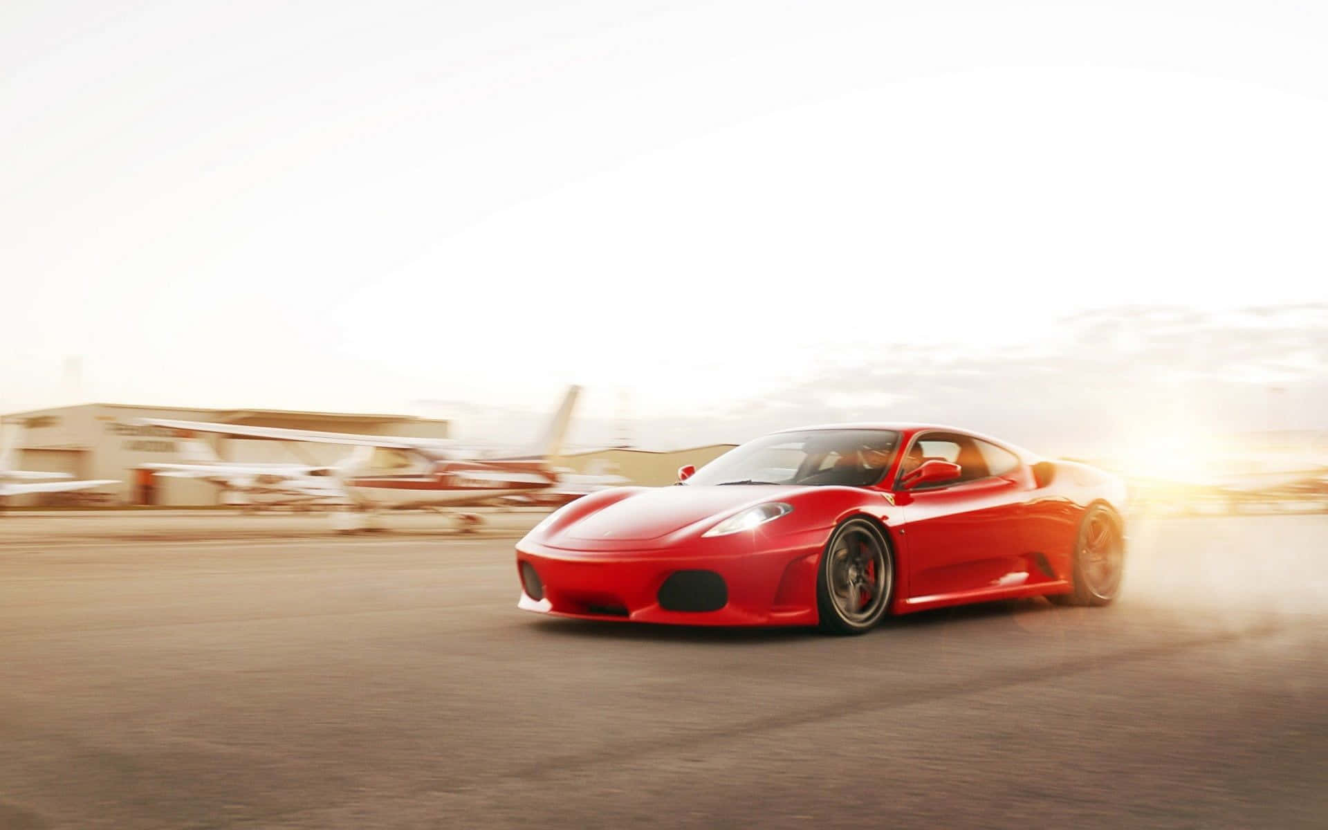 Ferrari F430 桌布 壁紙 — 一輛充滿活力的紅色法拉利跑車在柏油路上疾馳，帶有動態模糊效果，背後的金色陽光耀眼奪目。