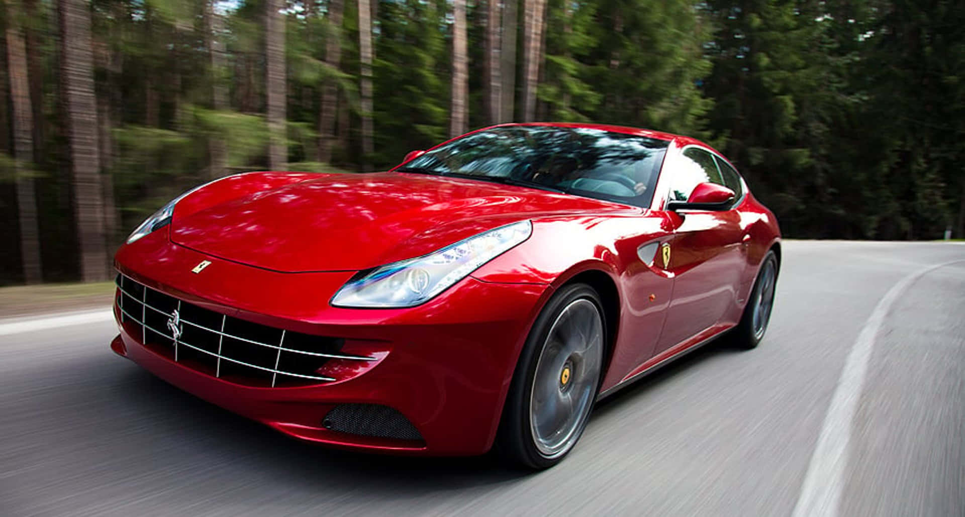 Ferrari Ff 桌布 壁紙 — 一輛充滿活力的紅色法拉利跑車在蜿蜒的林間道路上疾馳，動態模糊強調了其速度。