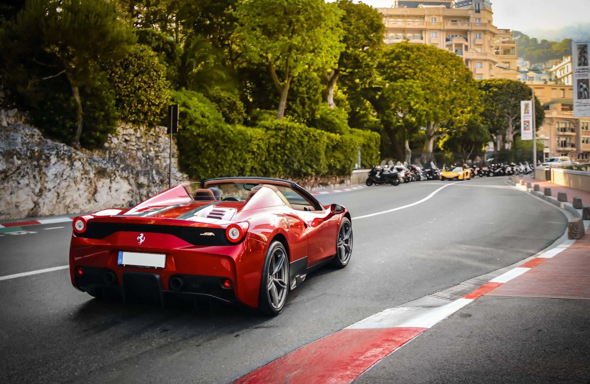Ferrari 458 Speciale 桌布 壁紙 — 一輛充滿活力的紅色法拉利跑車沿著蜿蜒的海岸公路行駛，兩旁是茂密的綠樹和優雅的建築。