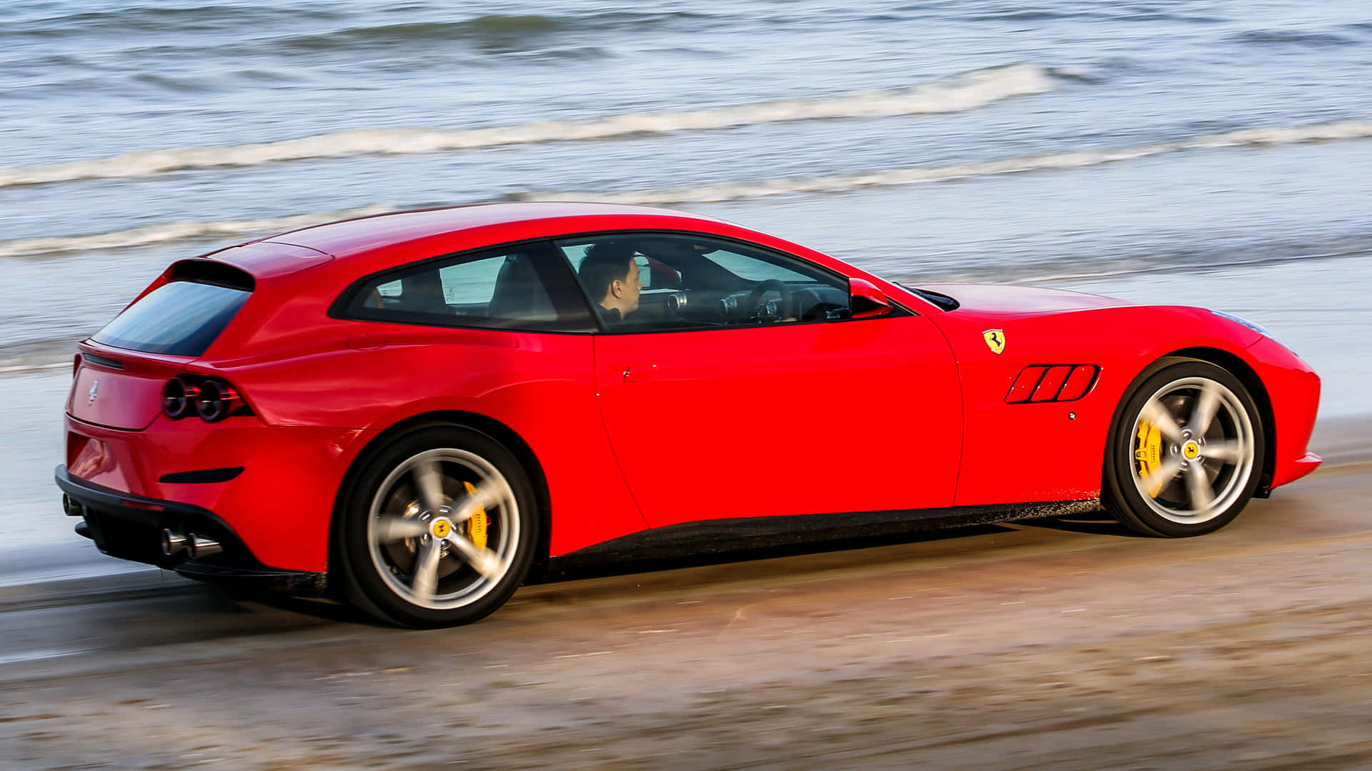 Ferrari Gtc4lusso 桌布 壁紙 — 一輛充滿活力的紅色法拉利跑車沿著濕沙灘疾馳，身後海浪拍打。