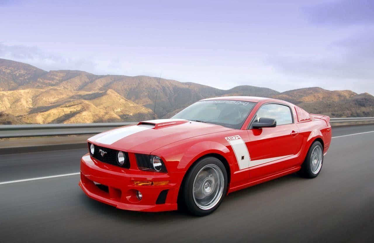 Ford Mustang Roush 桌布 壁紙 — 一輛充滿活力的紅色福特野馬GT在柔和暮色天空下，沿著高速公路奔馳，背景是乾燥的山脈。