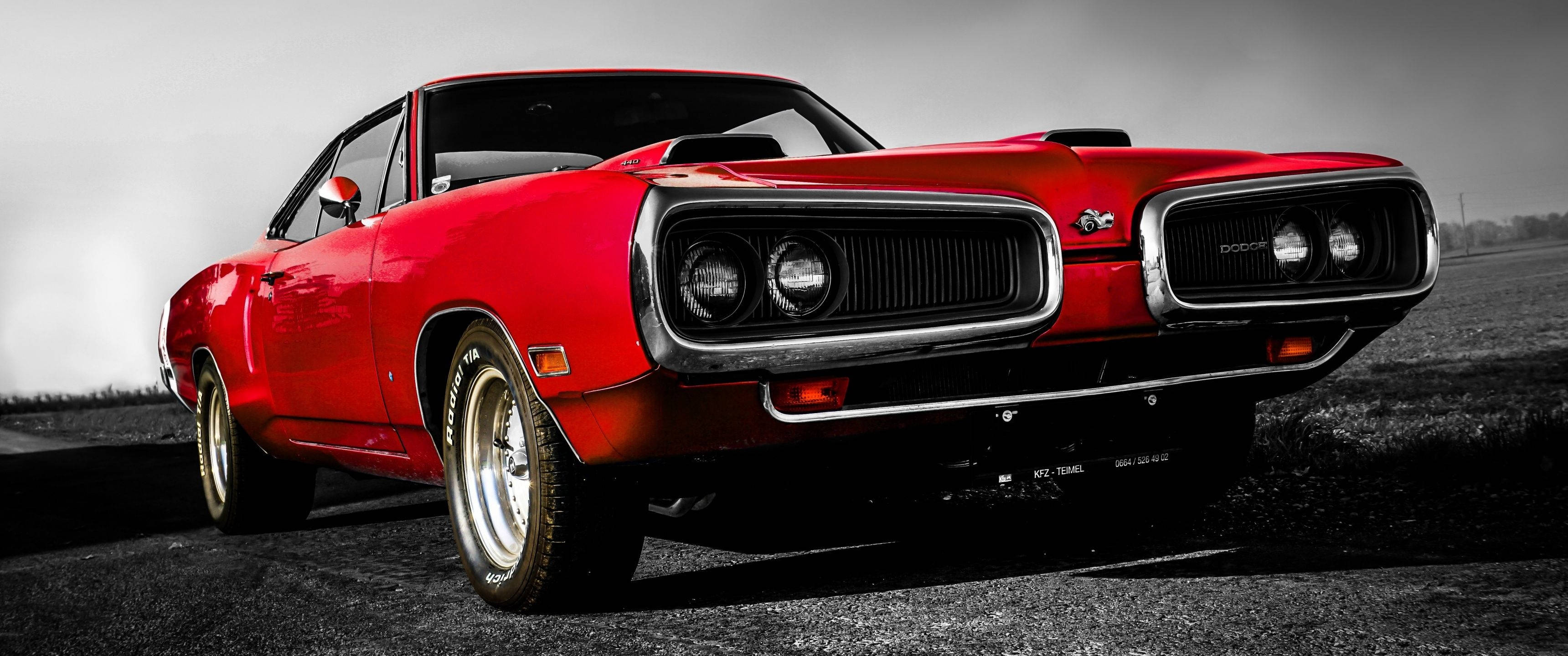 Dodge 桌布 壁紙 — 一輛充滿活力的紅色經典肌肉車，帶有鍍鉻細節，在陰沉天空下大膽地停在荒涼的道路上。