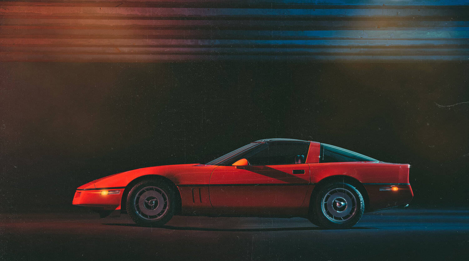 corvette 桌布 壁紙 — 一輛充滿活力的紅色經典跑車在霓虹燈閃爍的夜晚中滑行，身後拖曳著橙色和藍色的光帶。