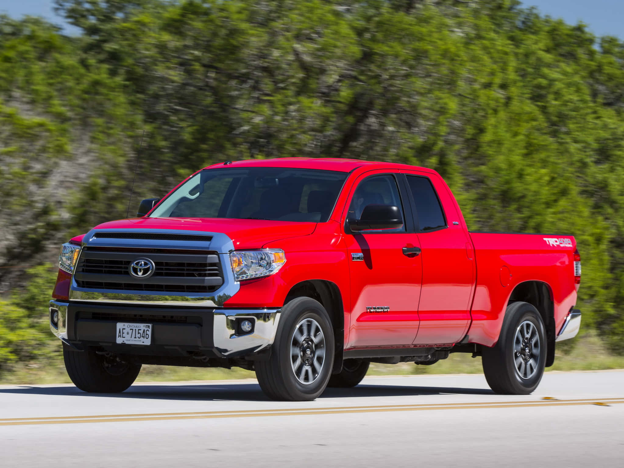 Toyota 桌布 壁紙 — 一輛充滿活力的紅色豐田Tundra TRD Pro皮卡在陽光明媚的高速公路上奔馳，背景中茂密的綠樹模糊不清。