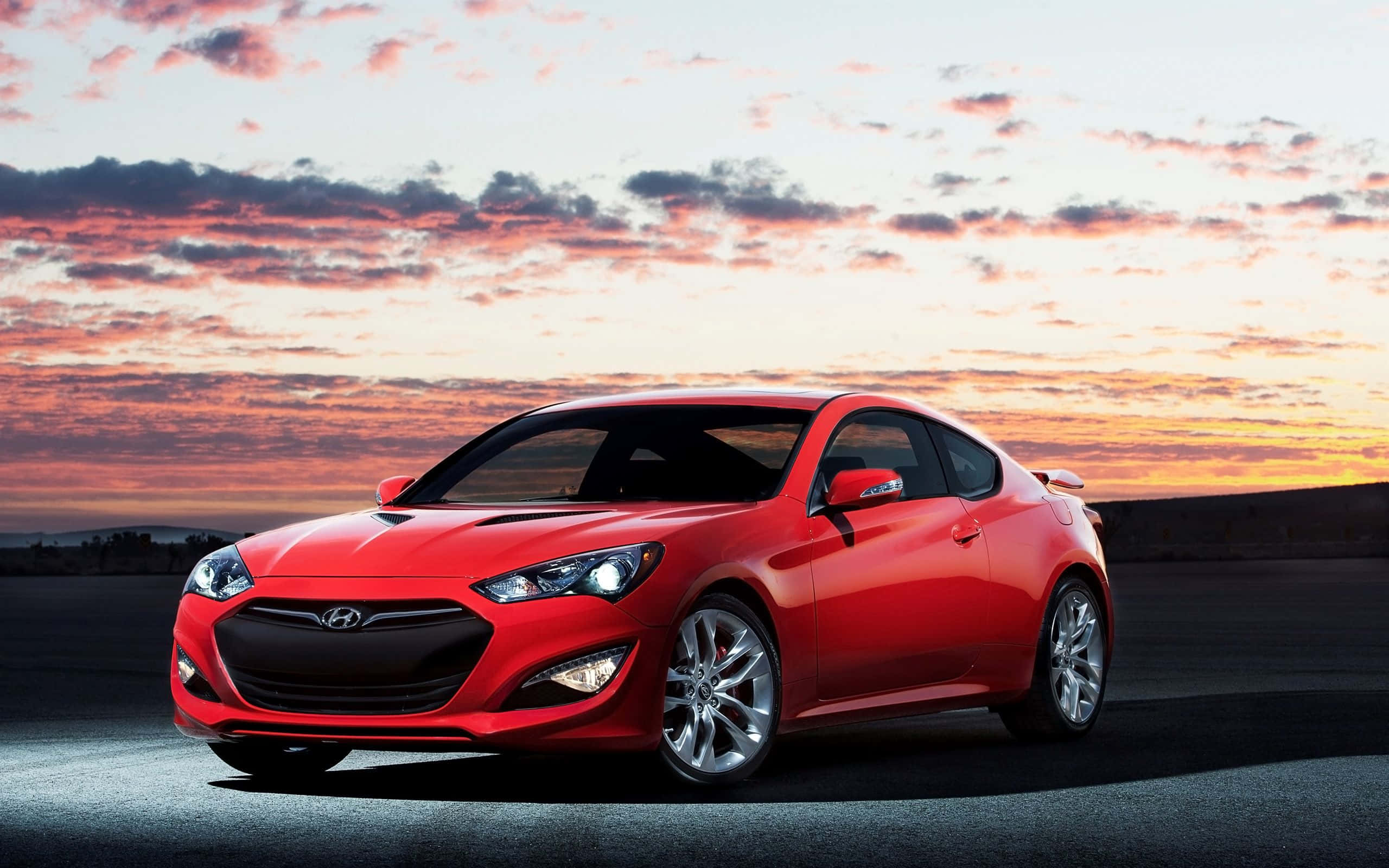 Hyundai Genesis 桌布 壁紙 — 一輛充滿活力的紅色跑車在壯麗的日落天空下閃耀，天空中有橙色和粉紅色的雲彩。