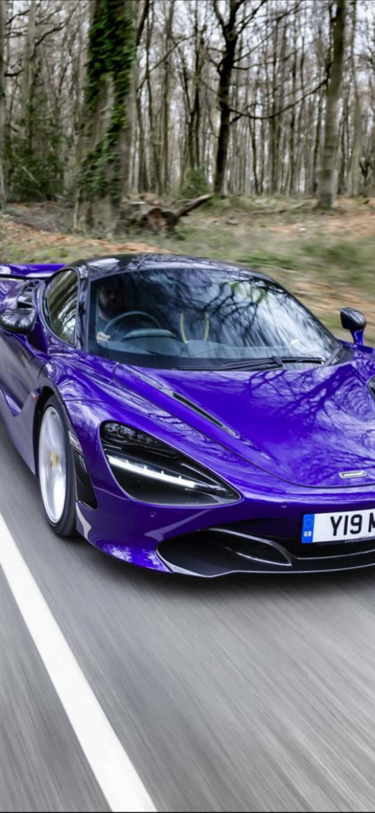 自然 桌布 壁紙 — 一輛充滿活力的紫色McLaren跑車沿著森林道路飛馳，背景有動態模糊和光禿的樹木。