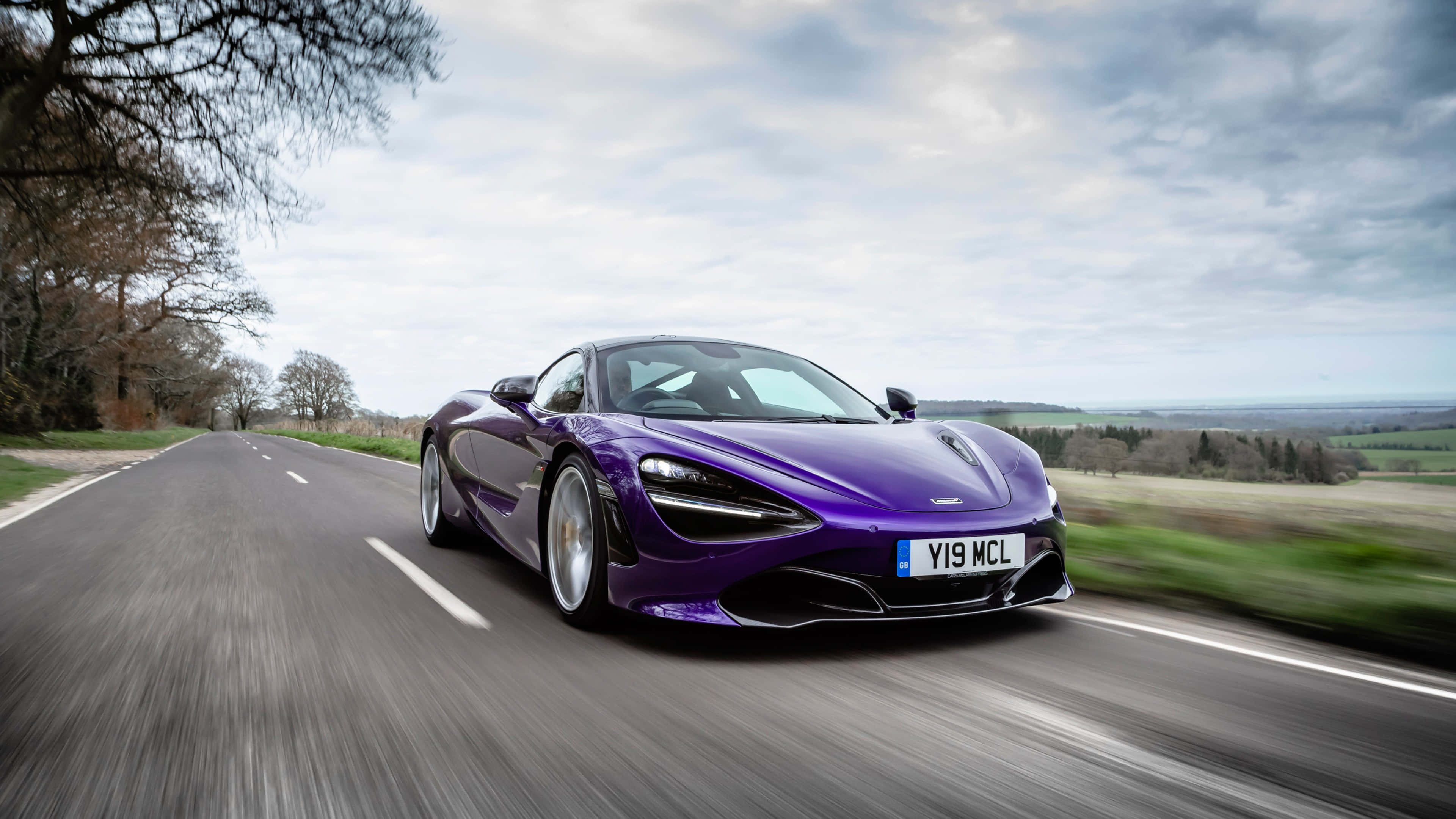 4K Mclaren 720s 桌布 壁紙 — 一輛充滿活力的紫色McLaren 720S在蜿蜒的鄉村道路上疾馳，帶有動態模糊和陰天。