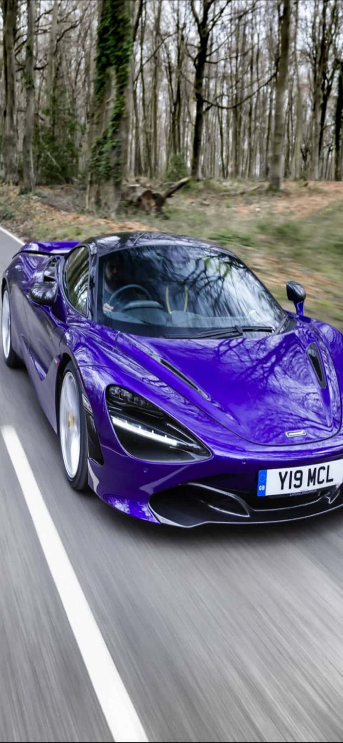 speeding car 桌布 壁紙 — 一輛充滿活力的紫色McLaren 720S在森林道路上疾馳，背景有動態模糊和光禿的樹木。