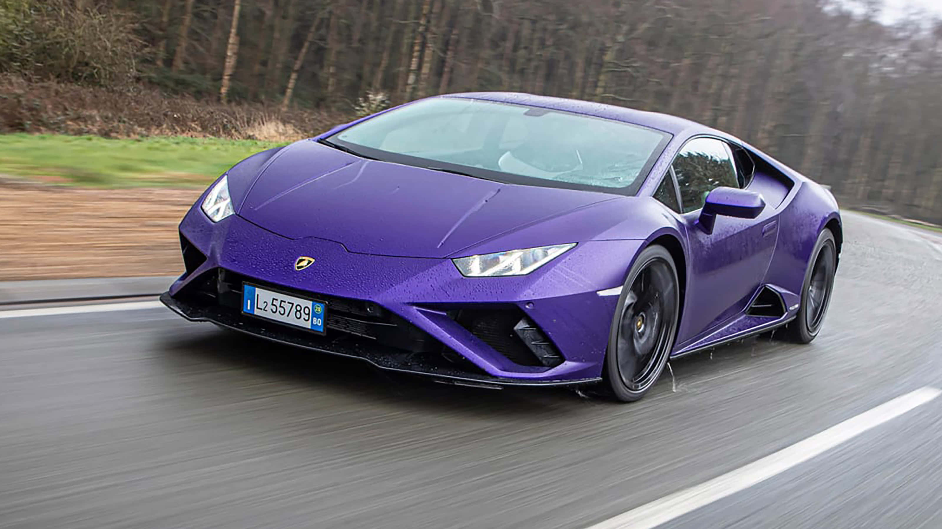 Cool Lamborghinis 桌布 壁紙 — 一輛充滿活力的紫色藍寶堅尼Huracán在樹林地區蜿蜒的道路上疾馳，帶有動態模糊效果。