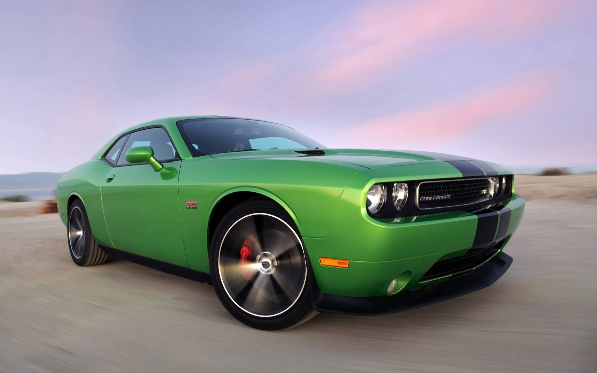 dodge iPhone 桌布 壁紙 — 一輛充滿活力的綠色 Dodge Challenger 帶有黑色條紋，在柔和的粉紫色暮色天空下，在沙漠公路上疾馳。