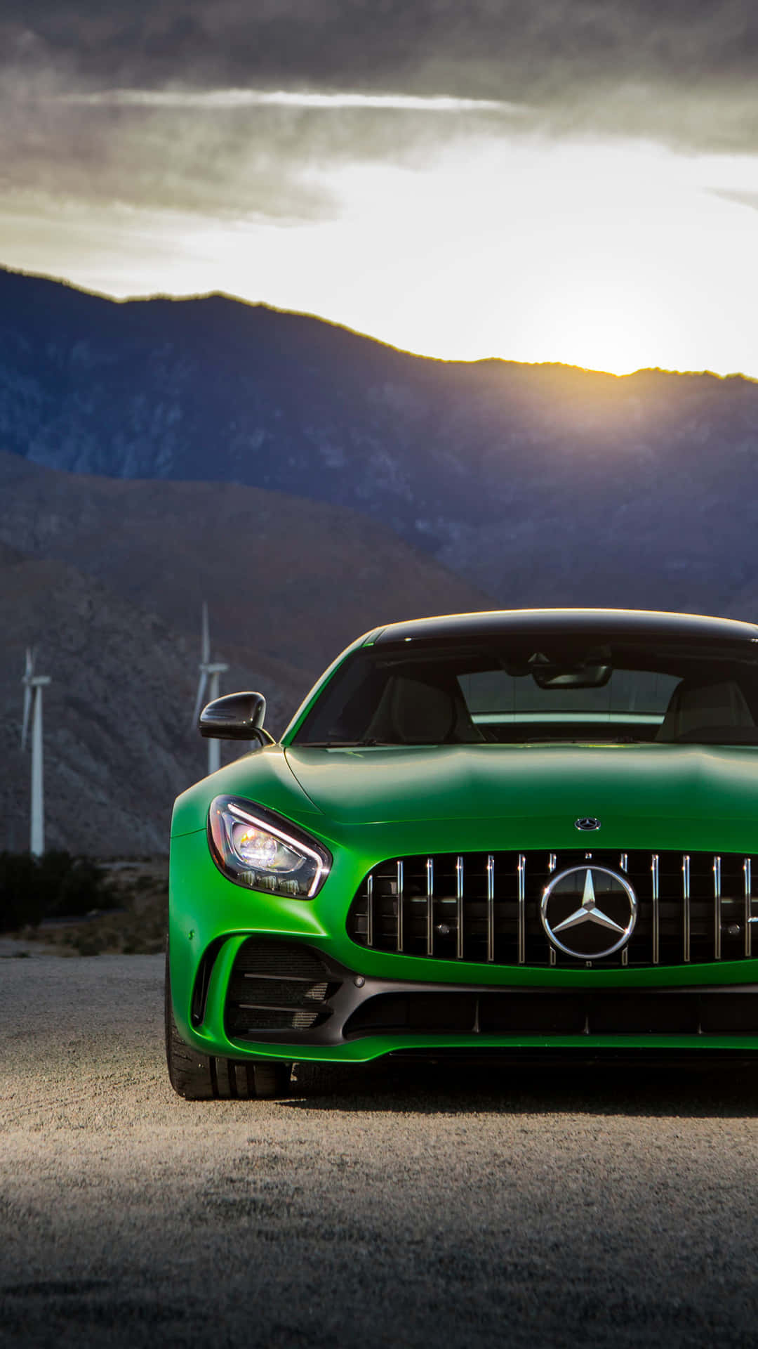 汽車 桌布 壁紙 — 一輛充滿活力的綠色 Mercedes-AMG GT 跑車停在沙漠公路上，背景有風力發電機和山脈，天空呈現戲劇性的日落景色。