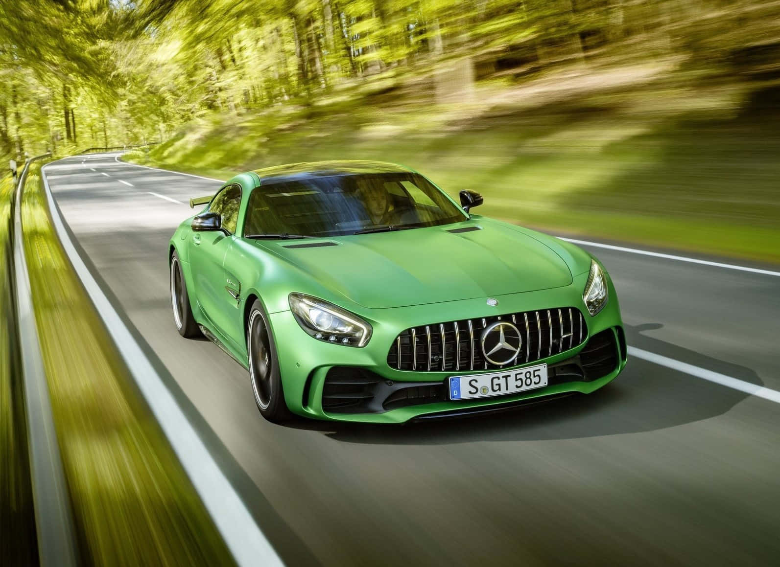 汽車 桌布 壁紙 — 一輛充滿活力的綠色 Mercedes-AMG GT S 沿著蜿蜒的森林道路飛馳，動態模糊強調了它的速度。