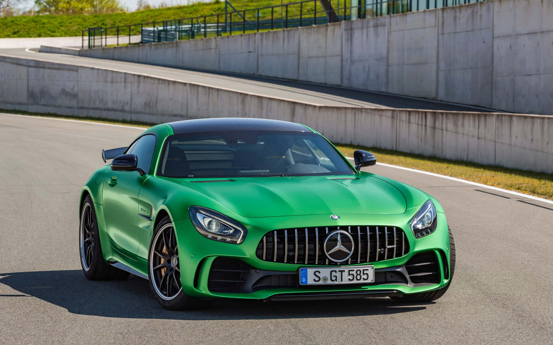汽車 桌布 壁紙 — 一輛充滿活力的綠色 Mercedes-AMG GT R 跑車停在陽光明媚的賽道上，背景有混凝土護欄和草坡。