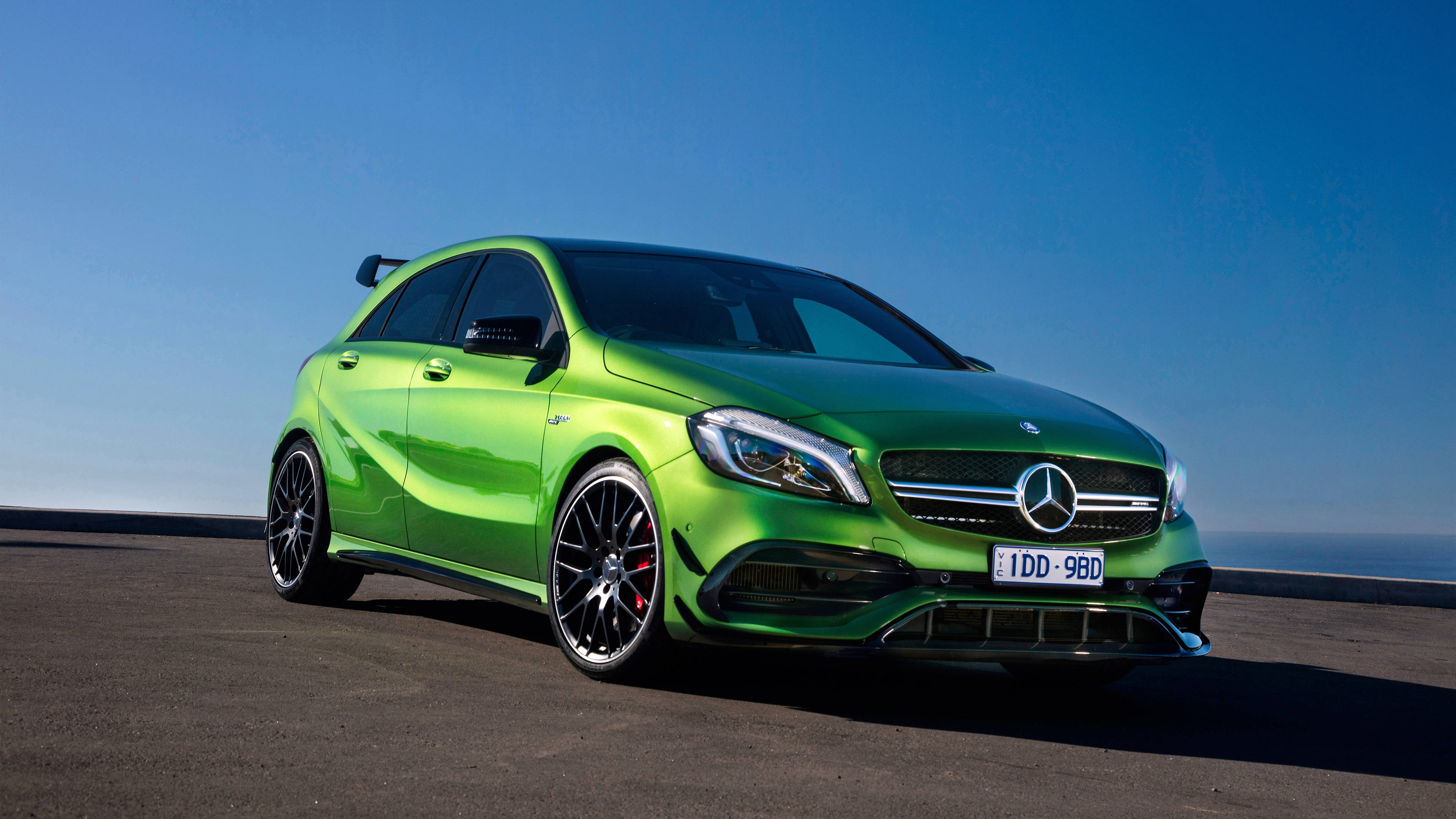 amg iPhone 桌布 壁紙 — 一輛充滿活力的綠色 Mercedes-AMG A45 S 跑車停泊在海岸公路上，天空清澈湛藍。