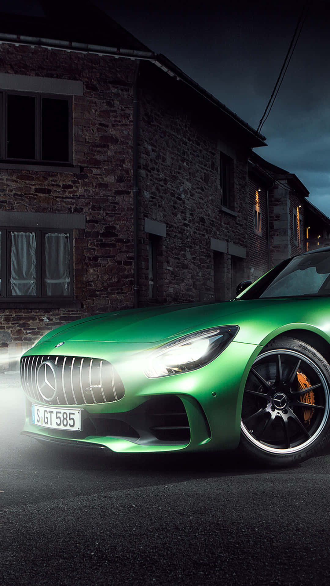Night Street 桌布 壁紙 — 一輛充滿活力的綠色 Mercedes-AMG GT 在夜間停放在一座質樸的石建築前，車頭燈閃閃發光。