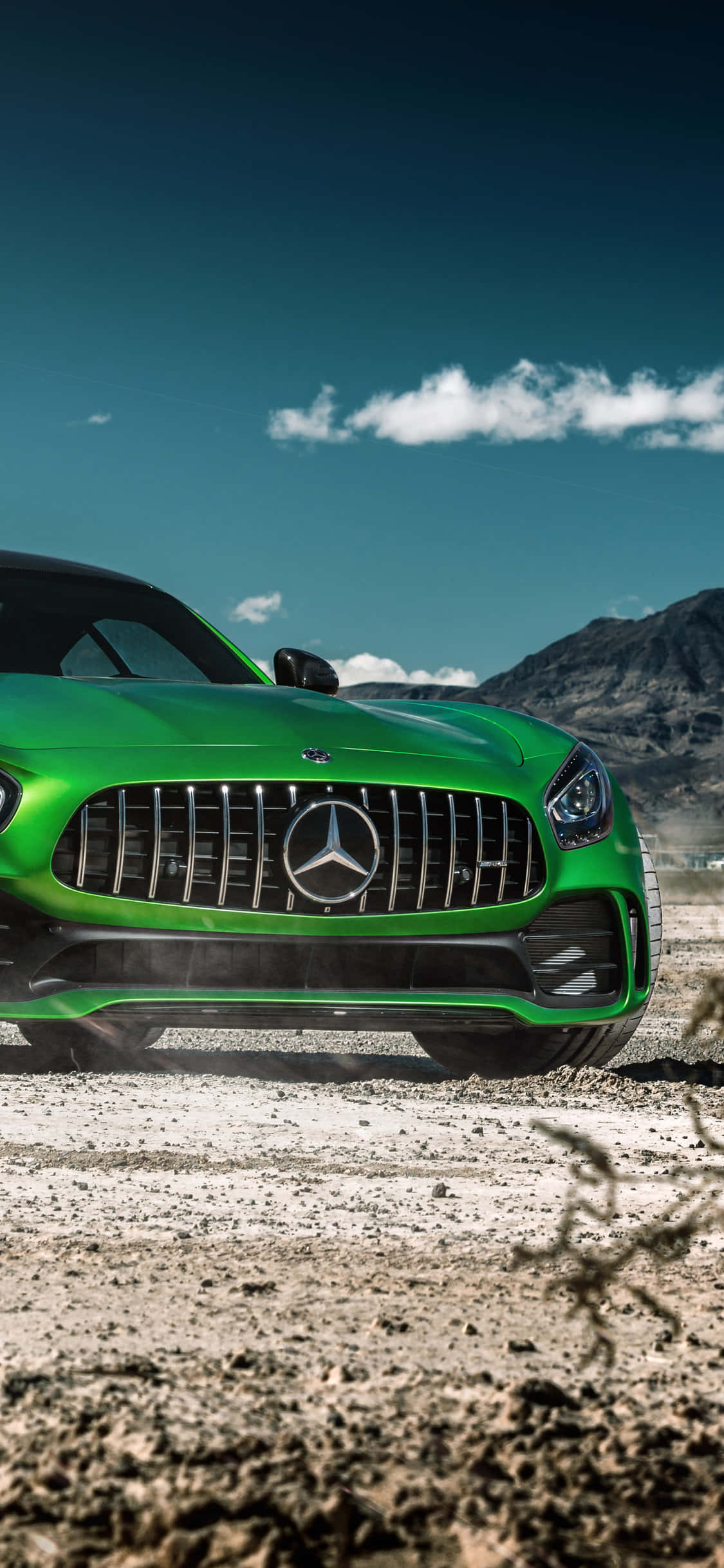 跑車 桌布 壁紙 — 一輛充滿活力的綠色 Mercedes-AMG GT 跑車停泊在塵土飛揚的地形上，背景有山脈和藍天。