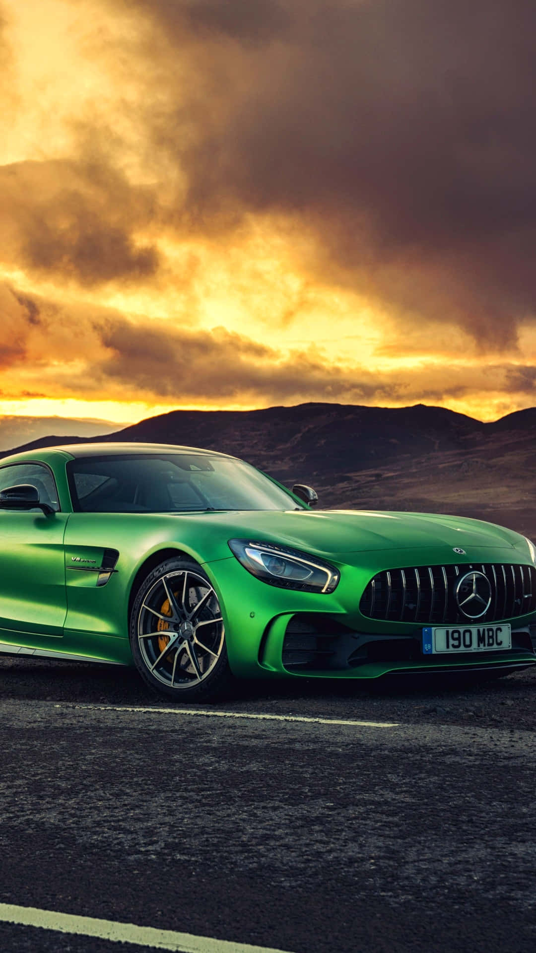 Yellow 桌布 壁紙 — 一輛充滿活力的綠色 Mercedes-AMG GT 跑車停泊在道路上，背景是戲劇性的金色日落天空和起伏的山丘。