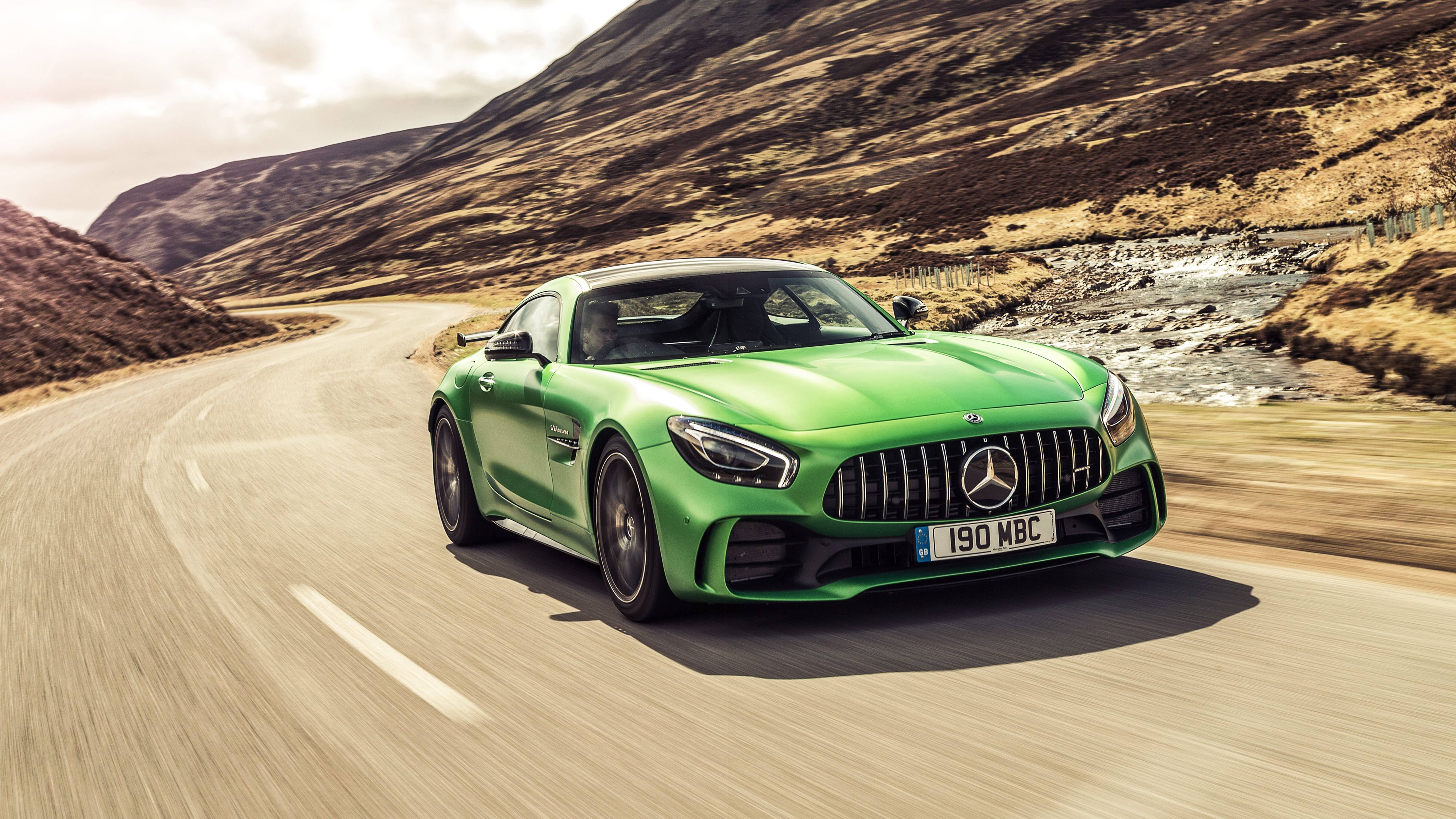 高畫質 賓士 桌布 壁紙 — 一輛充滿活力的綠色 Mercedes-AMG GT R 在晴朗的天空下，沿著蜿蜒的山路，在岩石溪流旁奔馳。