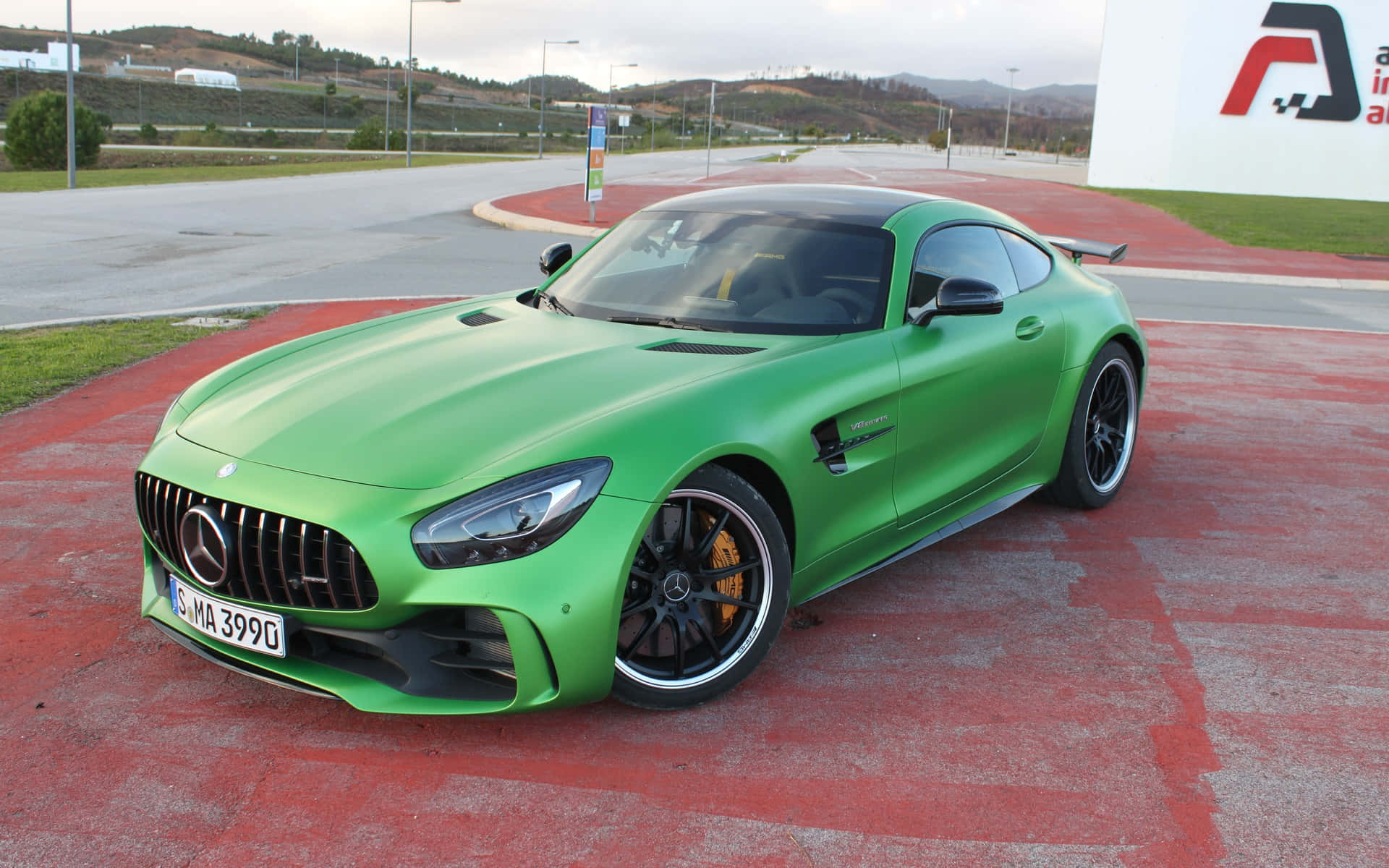 汽車 桌布 壁紙 — 一輛充滿活力的綠色 Mercedes-AMG GT R 跑車停在紅色瀝青路面上，背景有山丘。