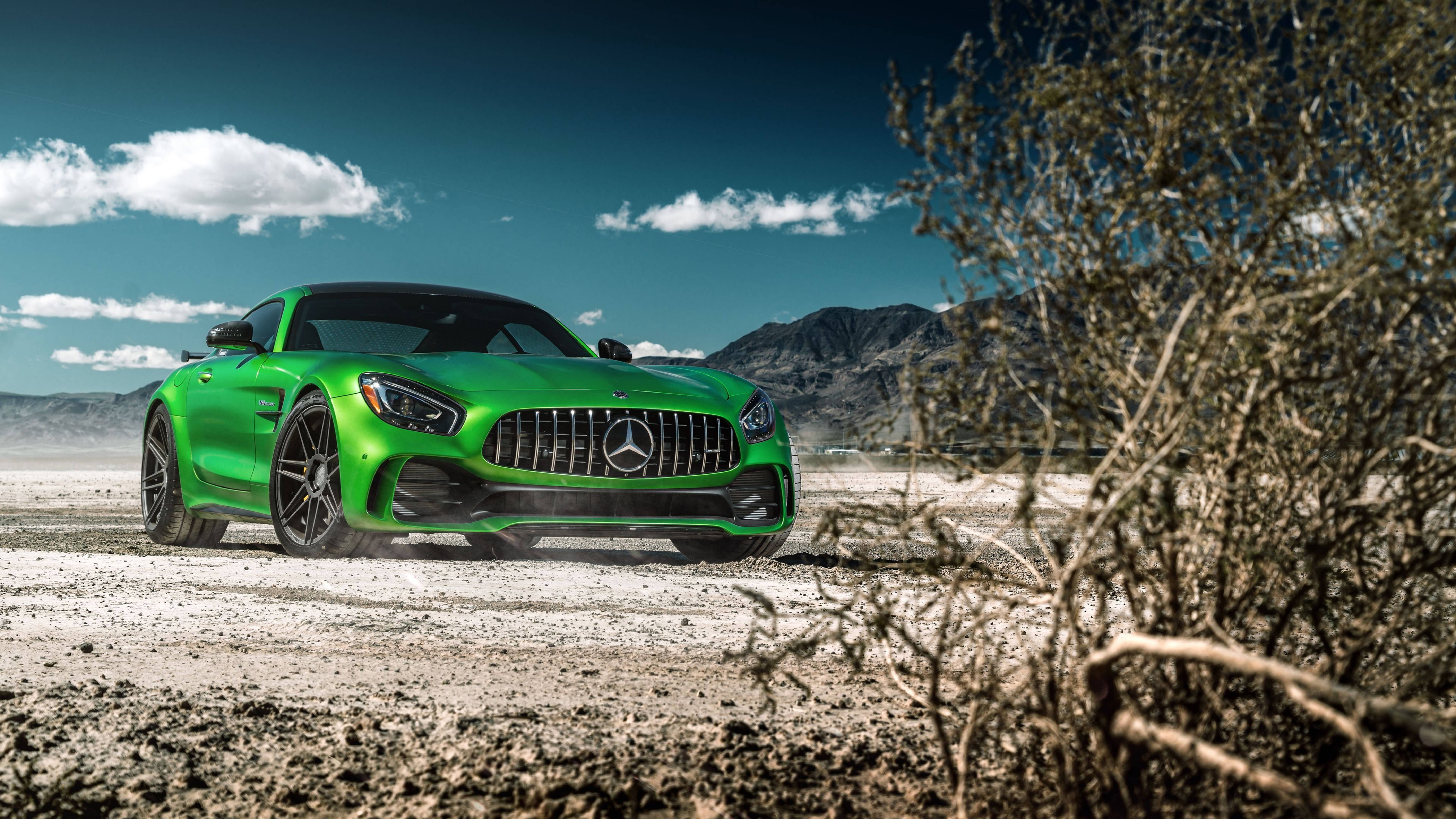 高畫質 賓士 桌布 壁紙 — 一輛充滿活力的綠色 Mercedes-AMG GT 跑車，在晴朗藍天和零星白雲下，疾馳過塵土飛揚的沙漠景觀。