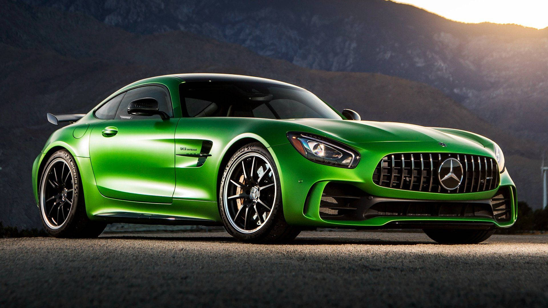 Mercedes 桌布 壁紙 — 一輛充滿活力的綠色 Mercedes-AMG GT 跑車在崎嶇的山地地形上，於金色夕陽下閃閃發光。