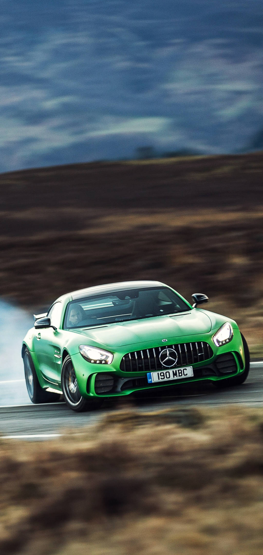 mercedes amg iPhone 桌布 壁紙 — 一輛充滿活力的綠色 Mercedes-AMG GT R 跑車在陰沉天空下，於蜿蜒道路上強勁飄移。
