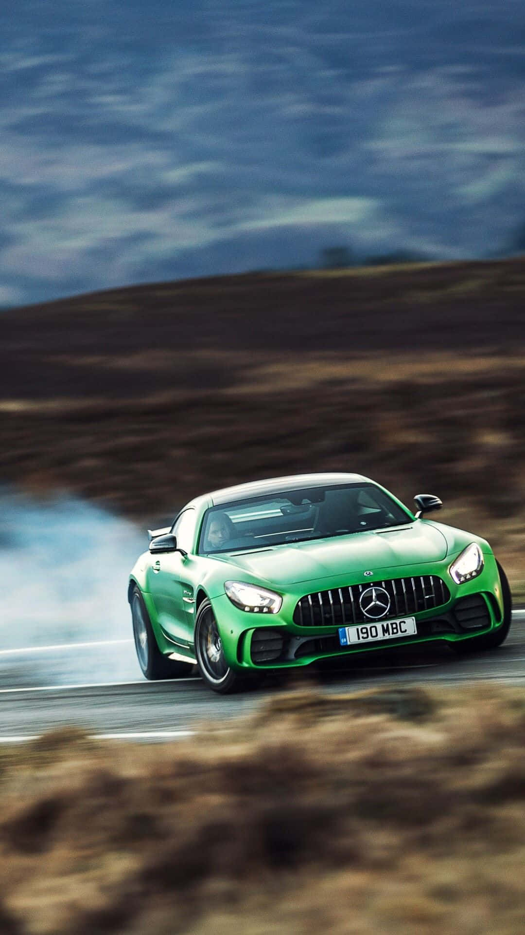 Mercedes 桌布 壁紙 — 一輛充滿活力的綠色 Mercedes-AMG GT S 在蜿蜒的道路上飄移，輪胎在陰天冒出滾滾濃煙。