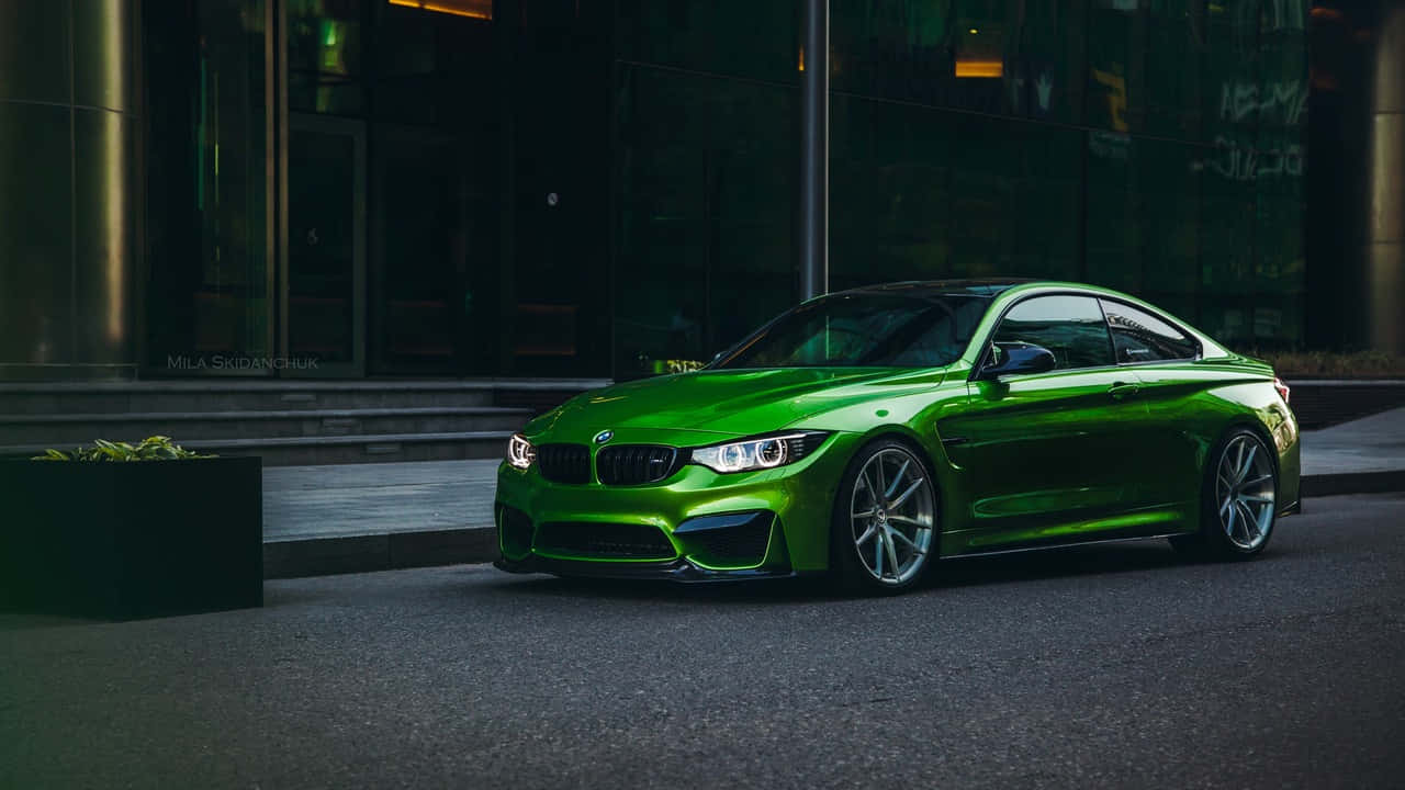 720p Bmw 桌布 壁紙 — 一輛充滿活力的綠色BMW M4雙門轎跑車在黃昏時分停在一棟現代玻璃建築旁，在城市的燈光下閃閃發光。