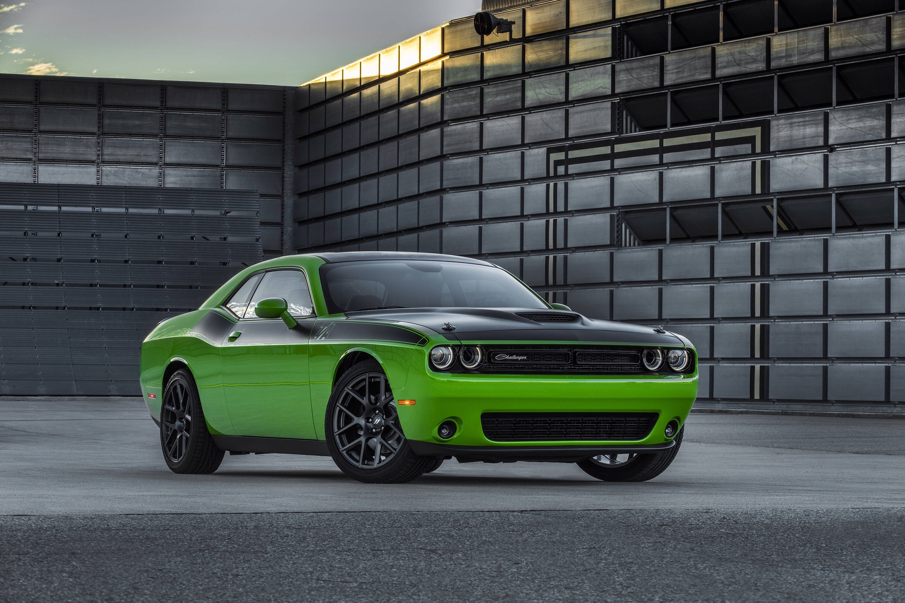Challenger 桌布 壁紙 — 一輛充滿活力的綠色Dodge Challenger，帶有黑色點綴，在黃昏時停在一座現代金屬建築前。