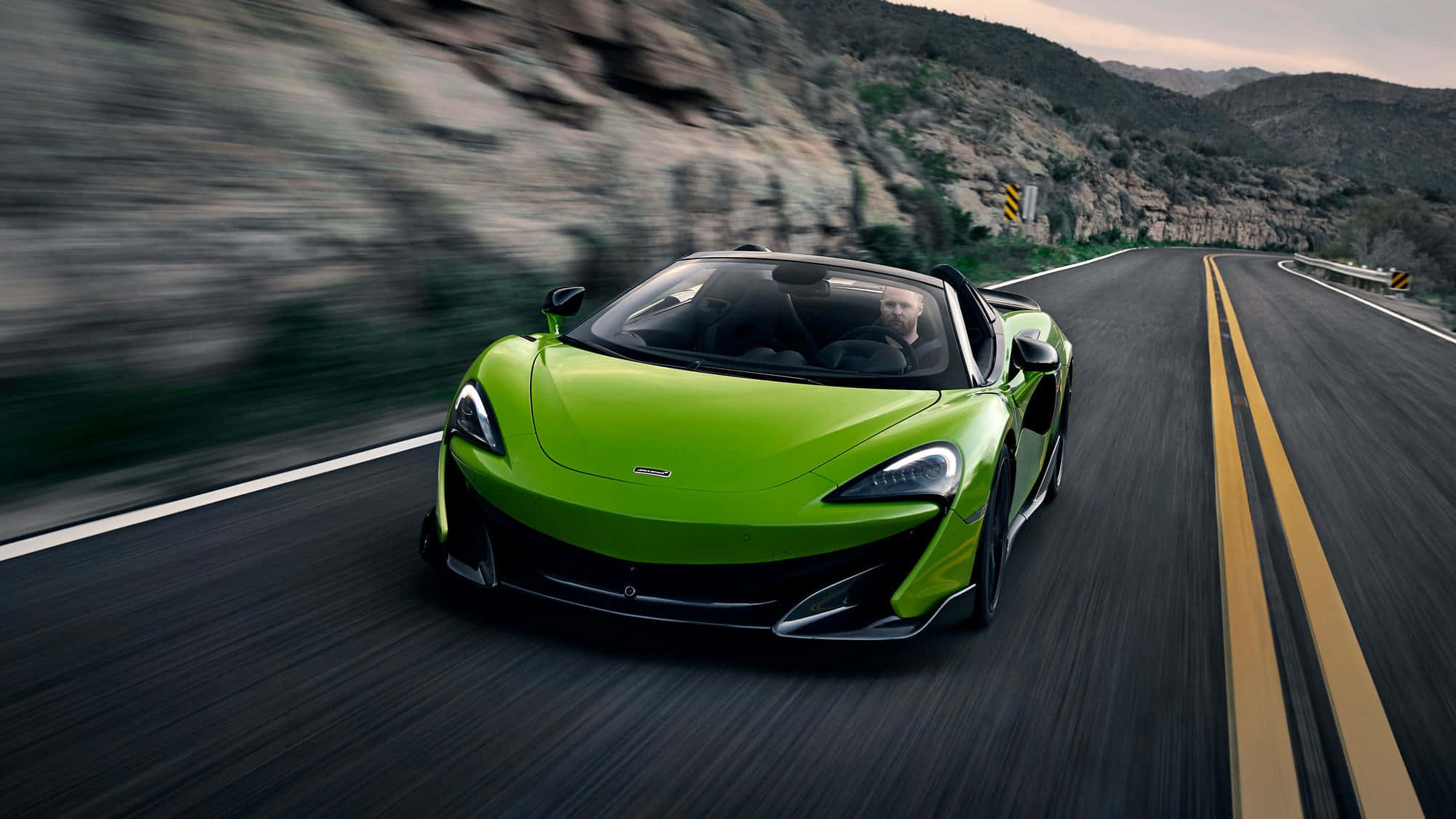Mclaren 600lt Spider 桌布 壁紙 — 一輛充滿活力的綠色McLaren跑車在蜿蜒的山路上奔馳，背景模糊。
