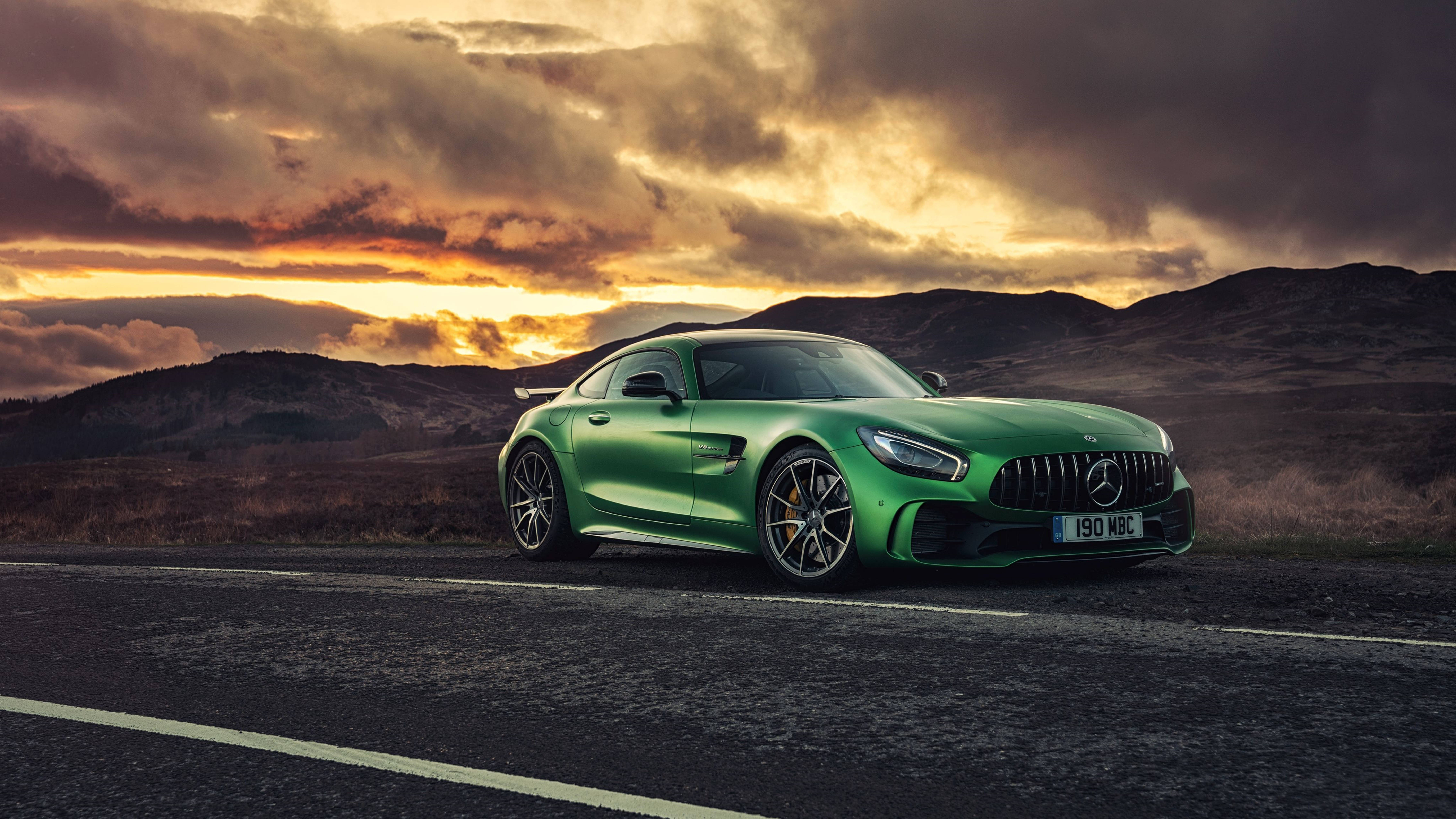 Mercedes 桌布 壁紙 — 一輛充滿活力的綠色Mercedes-AMG GT停泊在山路上，背景是戲劇性的日落天空和起伏的丘陵。