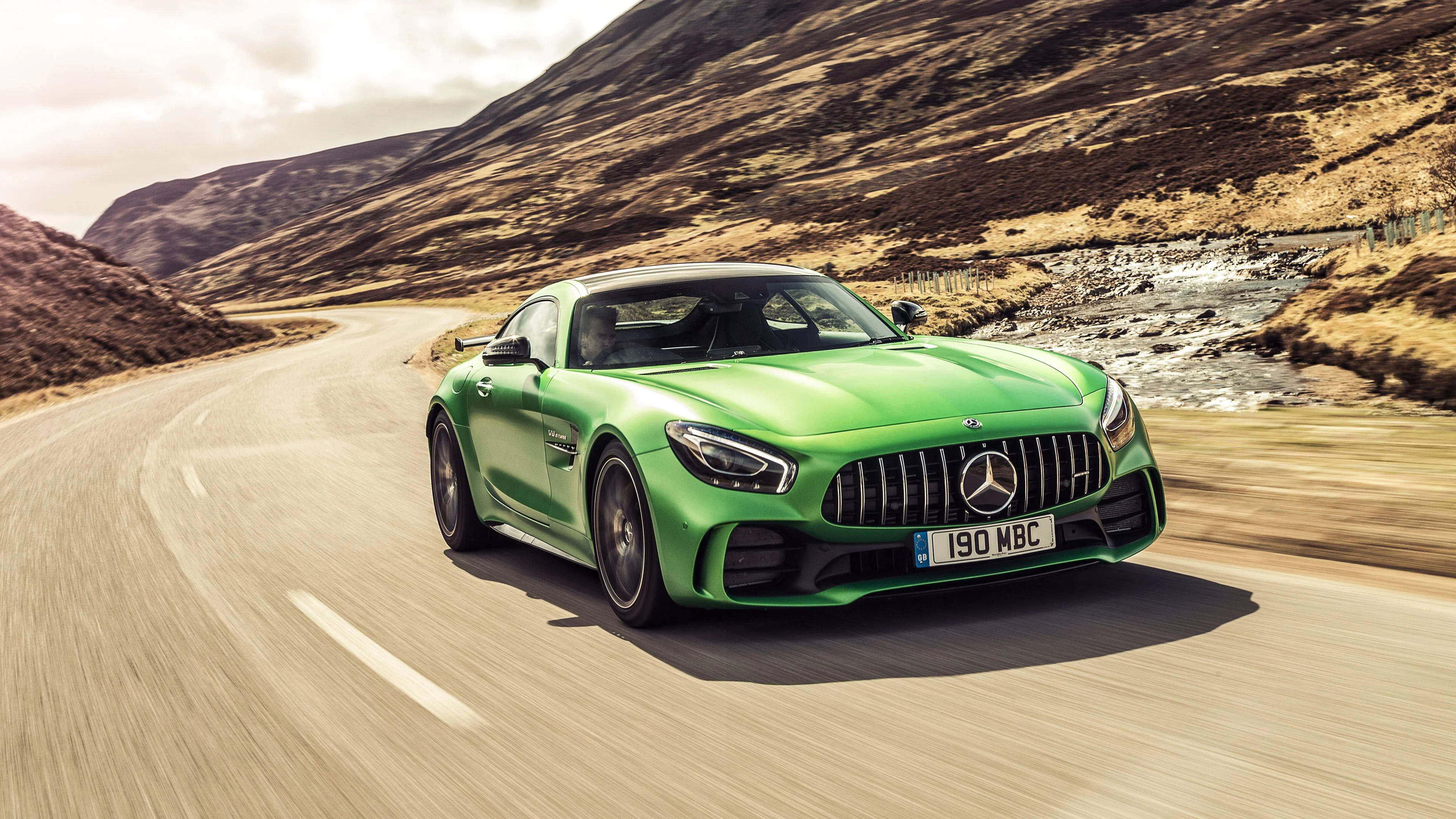 4K 奔馳壁紙 桌布 壁紙 — 一輛充滿活力的綠色Mercedes-AMG GT R在蜿蜒的山路上疾馳，背景是崎嶇的山丘和一條河流。