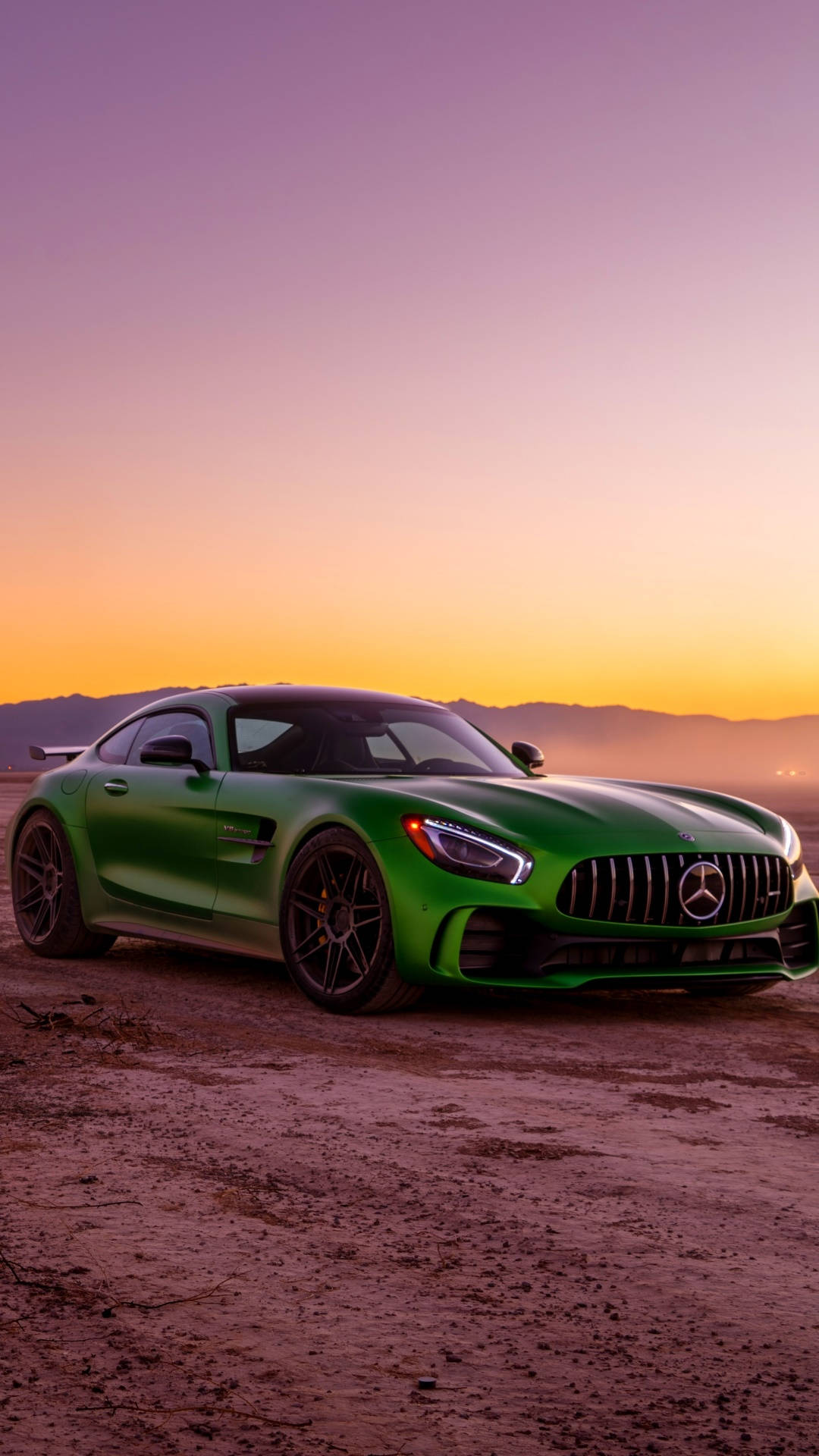 Amg 桌布 壁紙 — 一輛充滿活力的綠色Mercedes-AMG GT停泊在塵土飛揚的地形上，背景是漸變的日落天空和遠處的山脈。