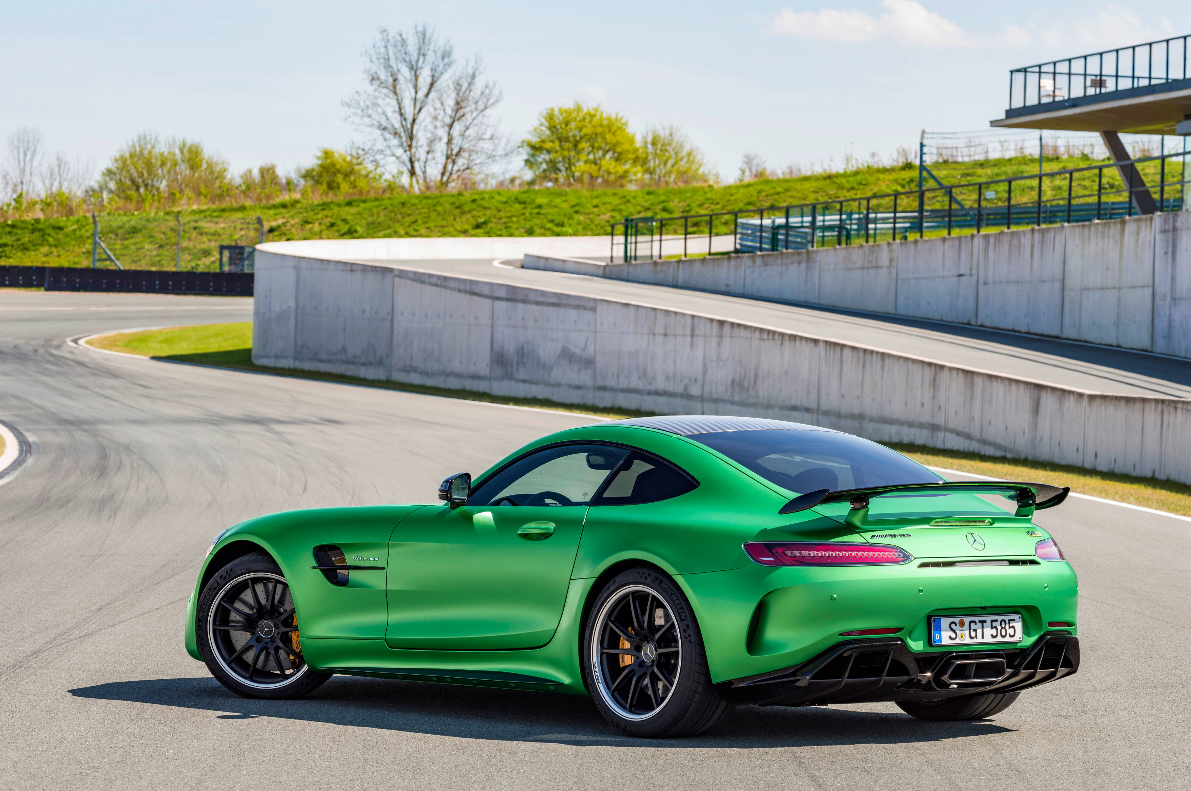跑車 桌布 壁紙 — 一輛充滿活力的綠色Mercedes-AMG GT S跑車在陽光明媚的賽道彎道上疾馳，賽道設有混凝土護欄和草地斜坡。