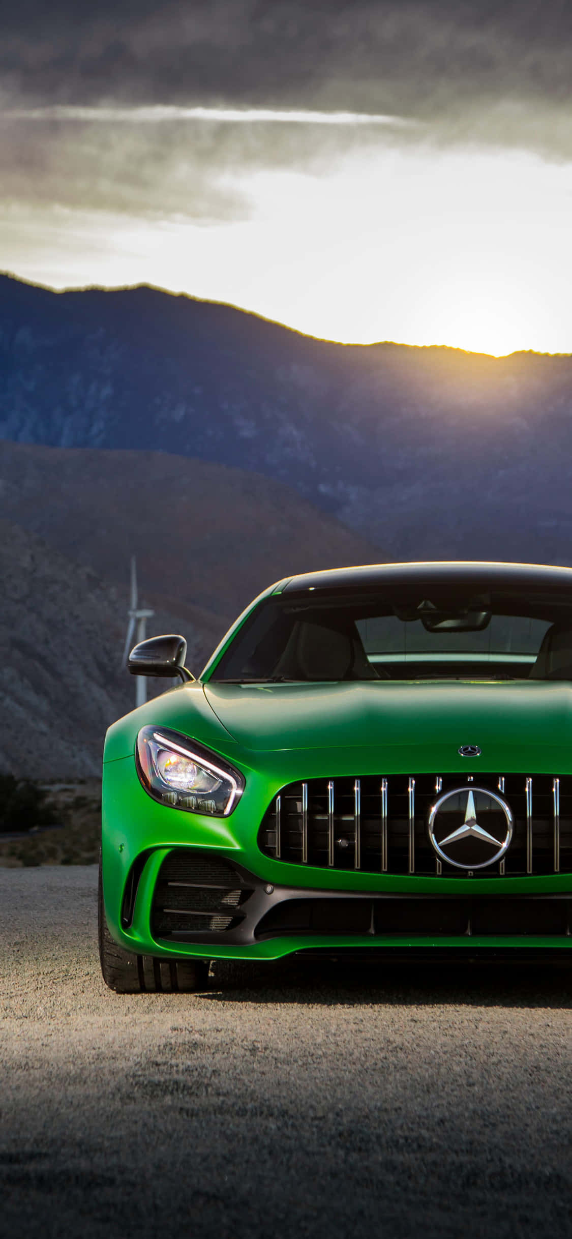 iPhone X Amg Gt-r 桌布 壁紙 — 一輛充滿活力的綠色Mercedes-AMG GT跑車停泊在山路上，夕陽西下，雲彩壯麗。