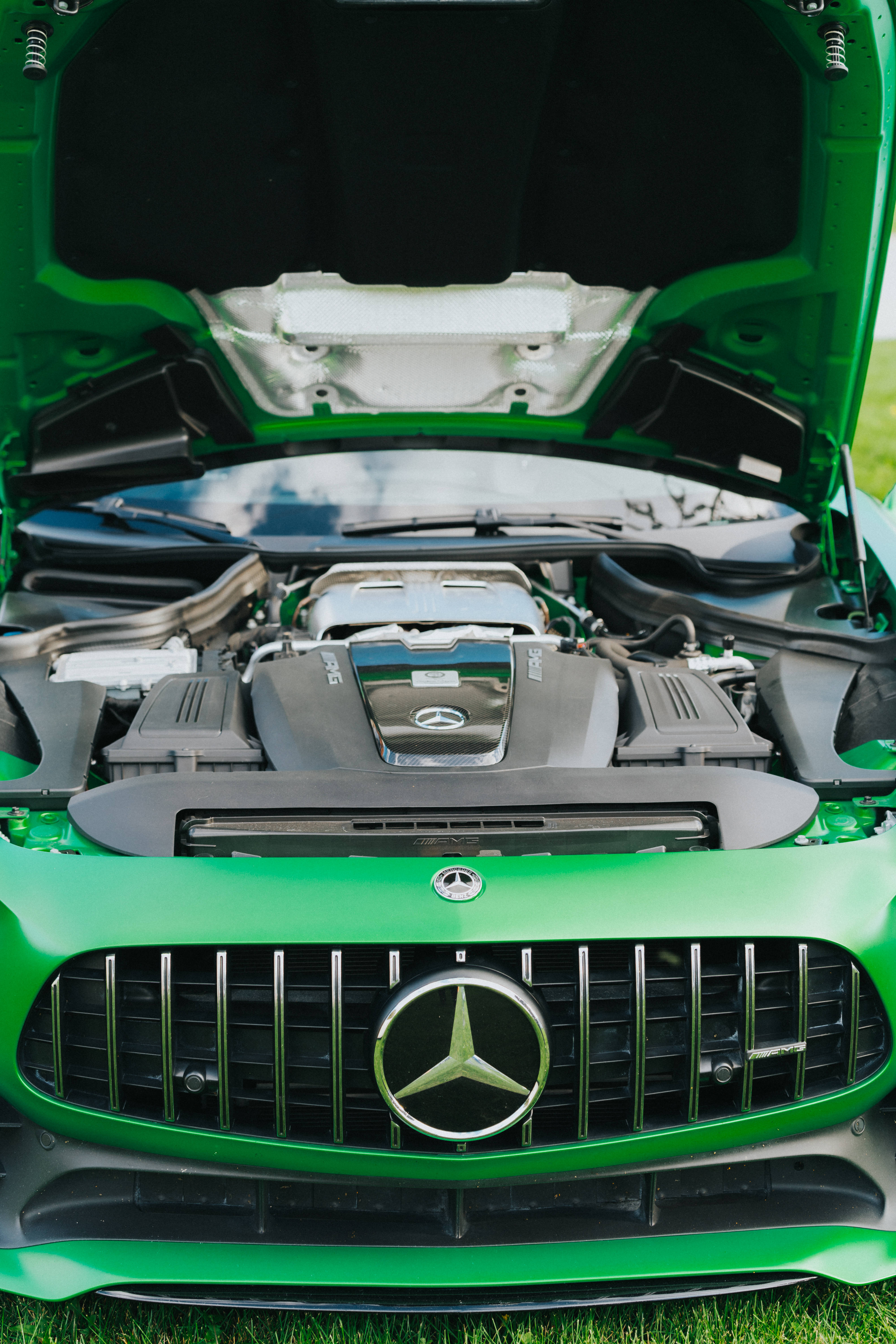 Mercedes Amg 桌布 壁紙 — 一輛充滿活力的綠色Mercedes-AMG跑車，引擎蓋打開，露出強勁的引擎，停在草地上。