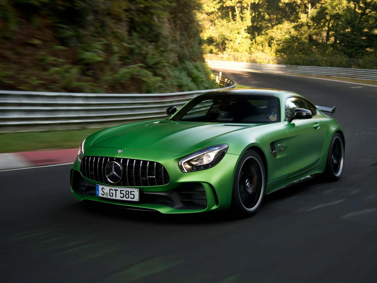 汽車 桌布 壁紙 — 一輛充滿活力的綠色Mercedes-AMG GT R沿著蜿蜒的森林道路疾馳，樹葉和護欄模糊不清。
