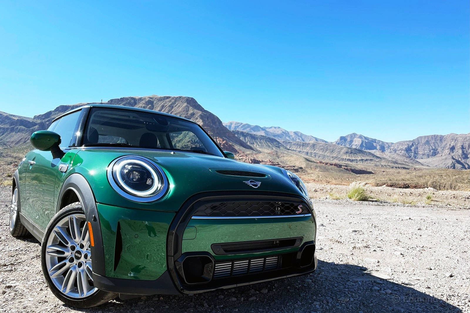 沙漠 桌布 壁紙 — 一輛充滿活力的綠色MINI Cooper S停泊在陽光明媚的沙漠碎石路上，背景是崎嶇的山脈和清澈的藍天。