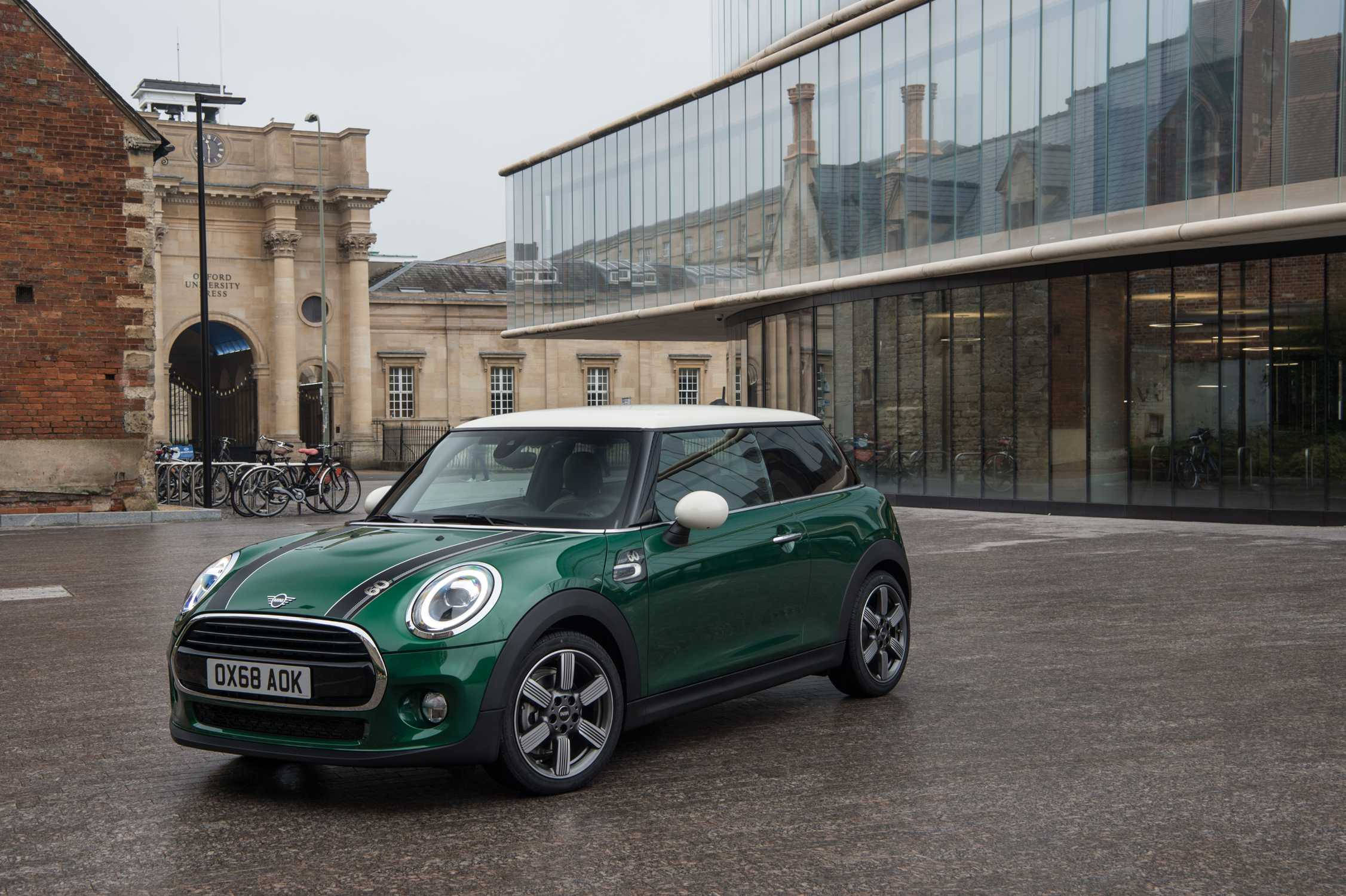 城市 桌布 壁紙 — 一輛充滿活力的綠色MINI Cooper，白色車頂，停在濕漉漉的路面上，前方是歷史石拱門和現代玻璃建築。