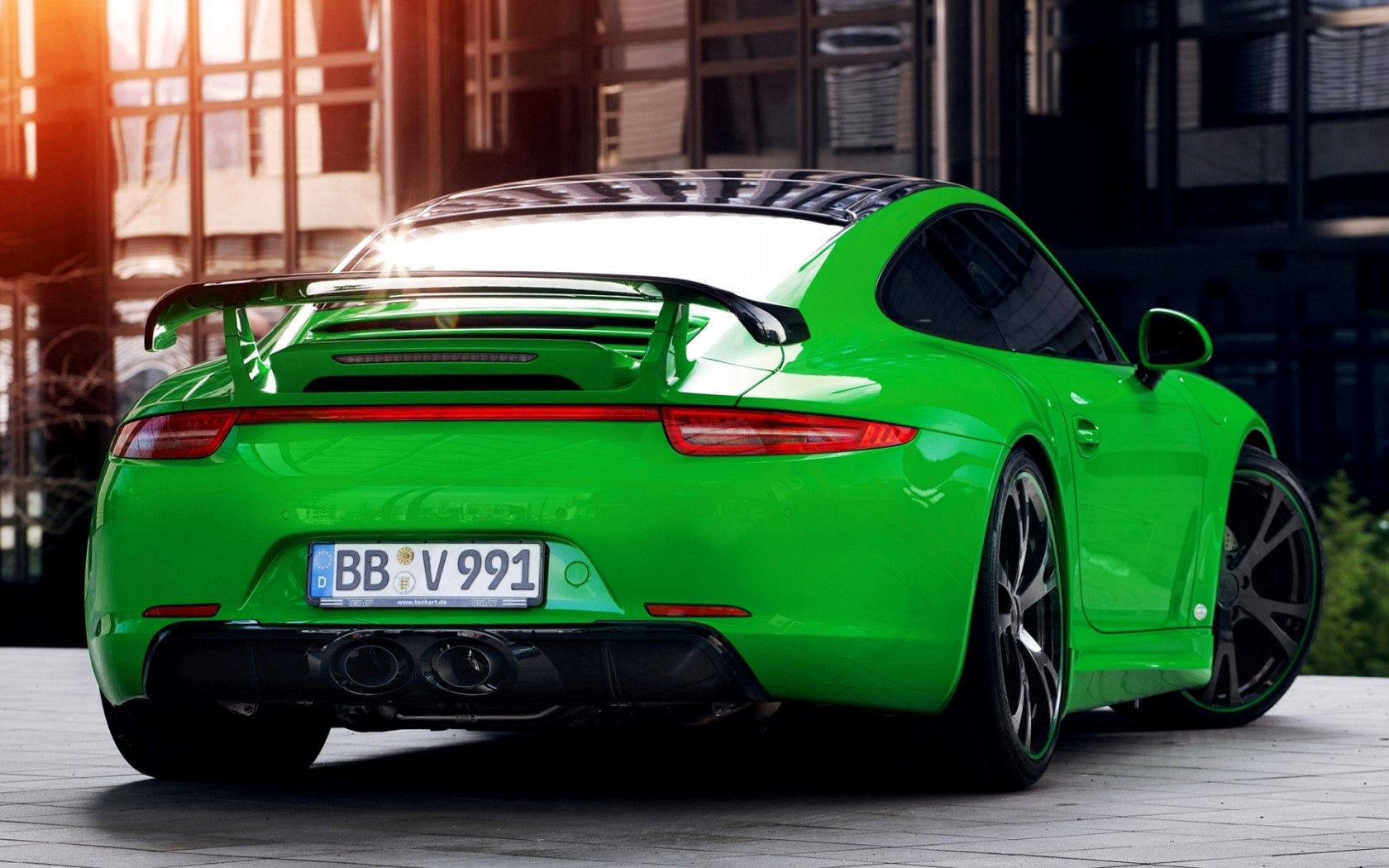 保時捷 桌布 壁紙 — 一輛充滿活力的綠色保時捷 911 GT3 RS 在現代玻璃建築背景下，於黃金時段的陽光下閃閃發光。